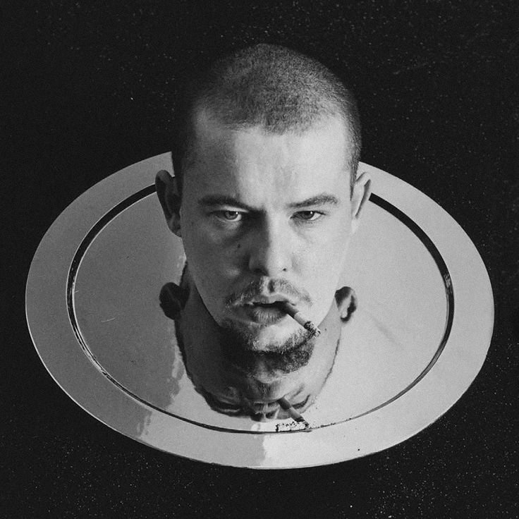 Black and white portrait of a man’s severed head illusion on a silver platter, cigarette in mouth — a haunting and surreal tribute to Alexander McQueen’s provocative artistry and fascination with death, identity, and spectacle.