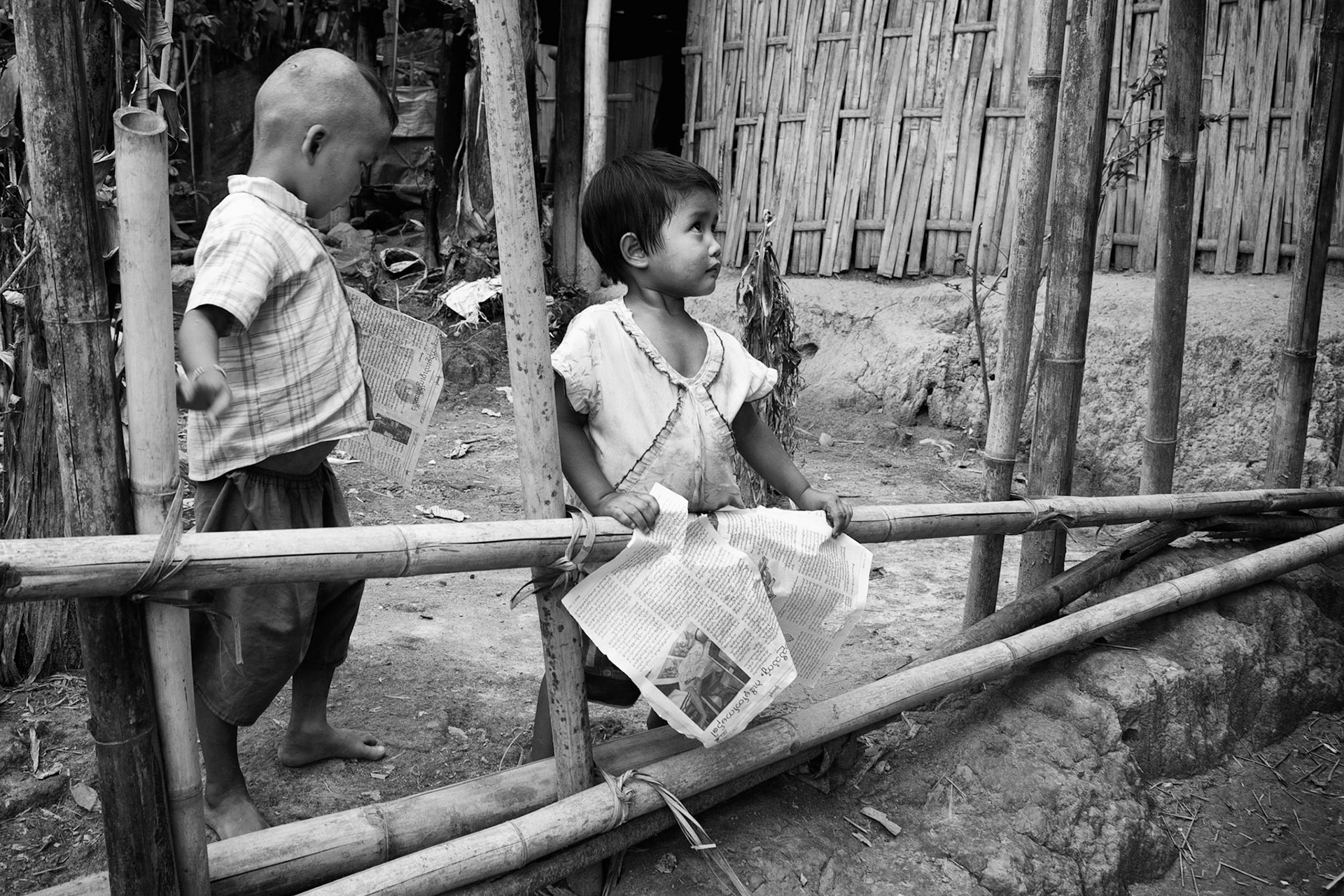 Two Burmese Karen refugee children (Boy and Girl) carrying old newspaper.