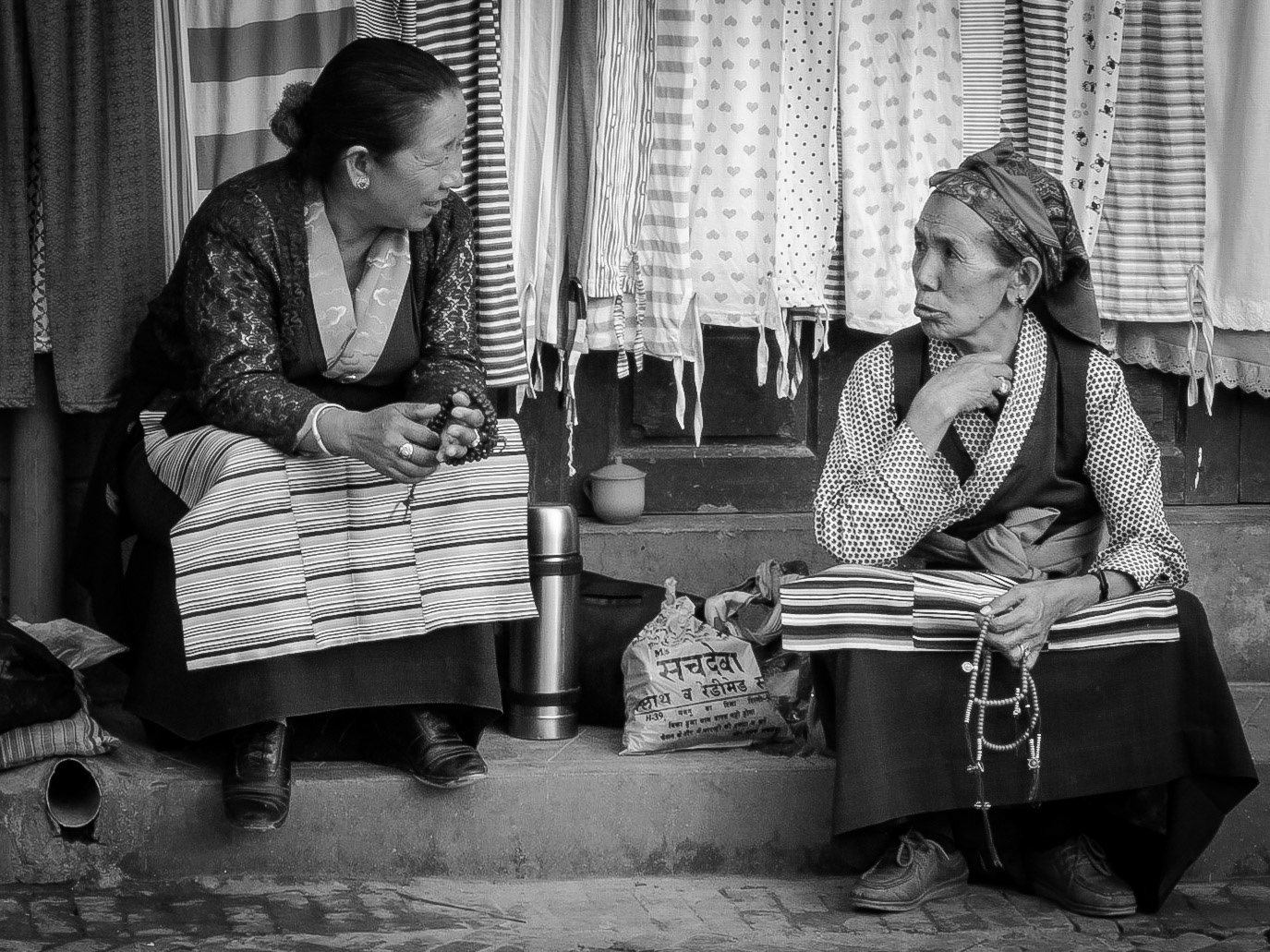 Two Nepali women in tradition dress chat while seated on the steps outside thier shop in Kathmandu.