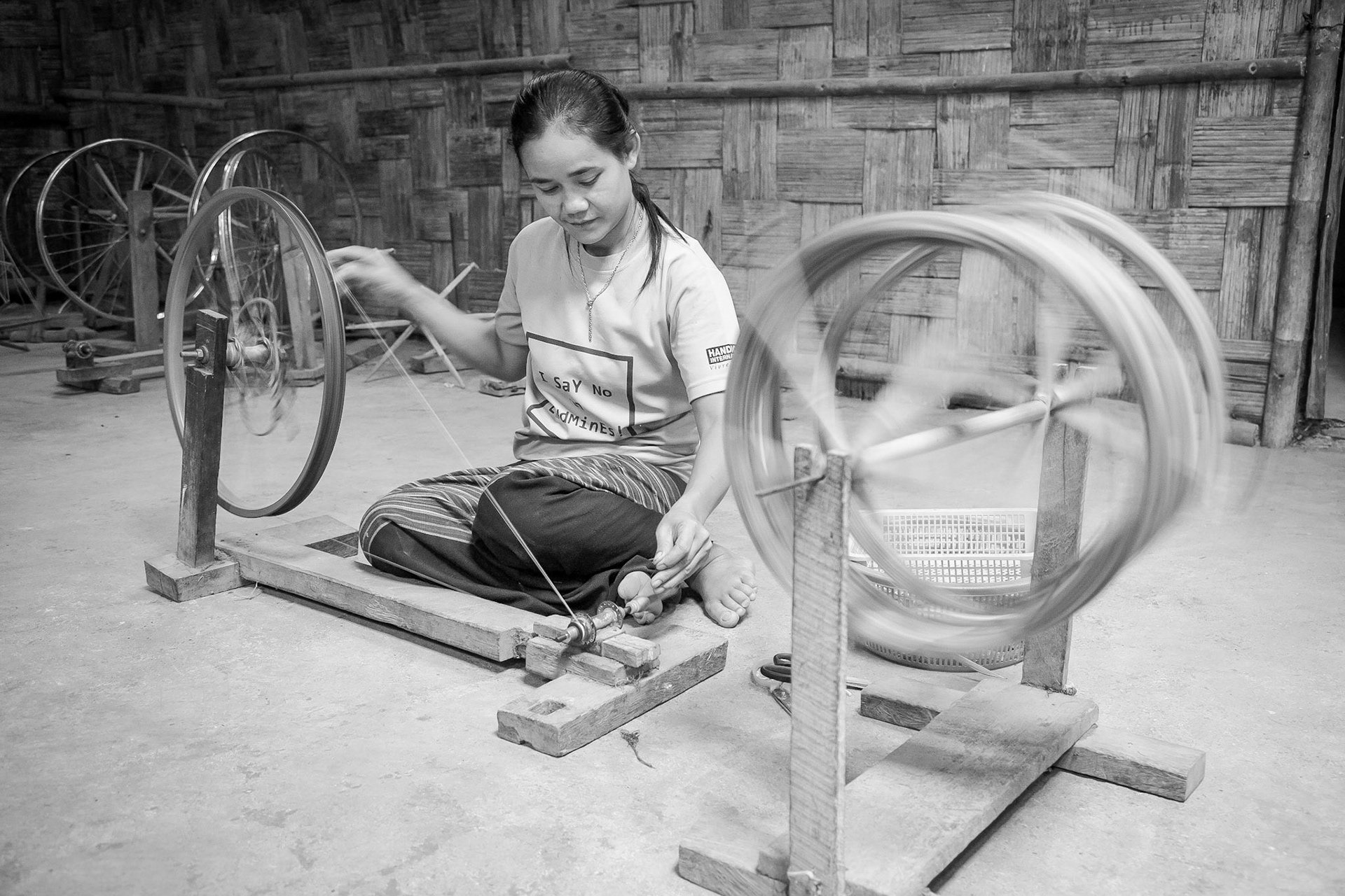 Female Burmese Karen refugee, in Tham Hin camp, learns to spin yarn on rudimentary spinning wheel.