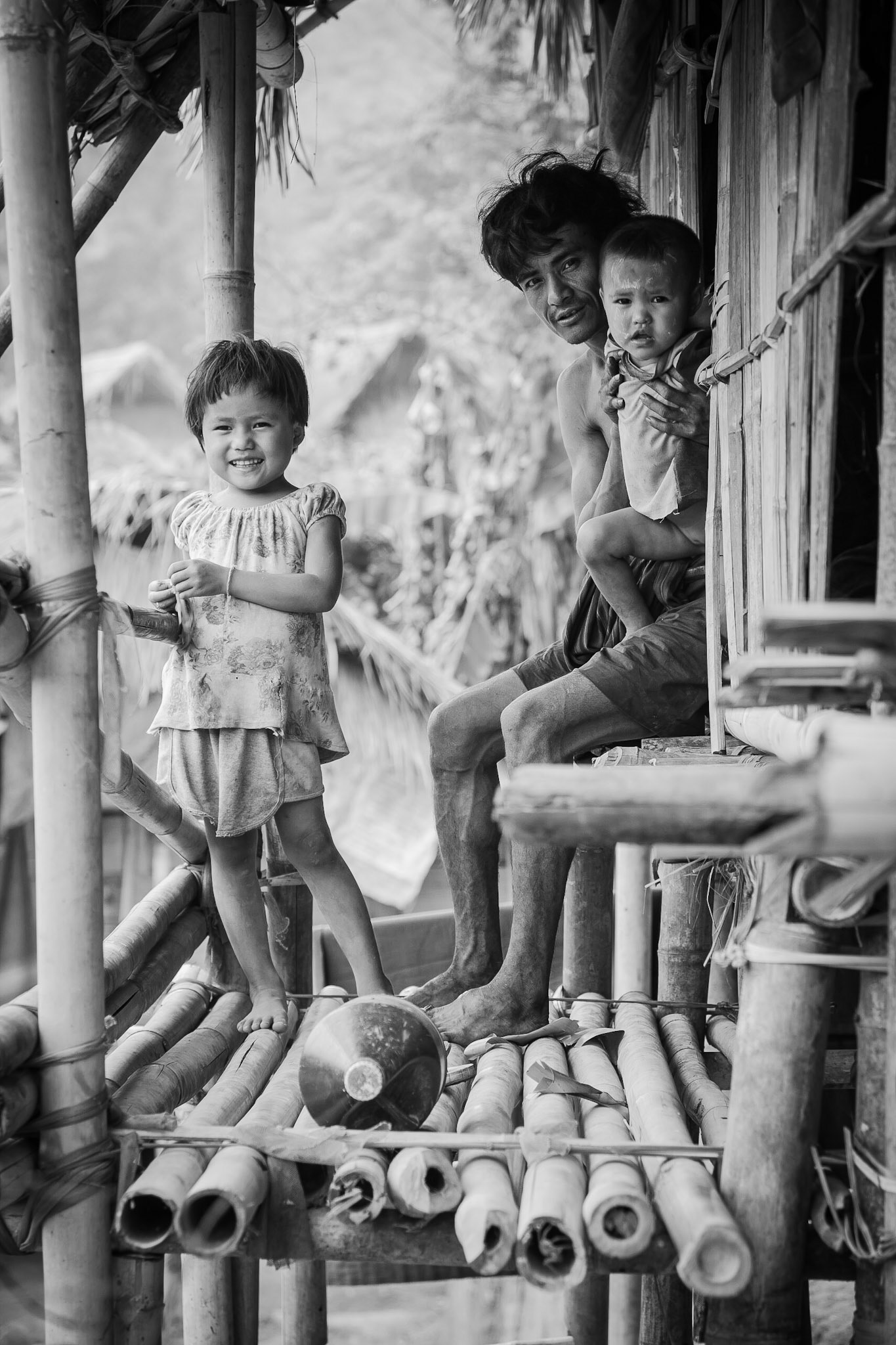 Burmese karen refugee family (Father, baby and young girl) sitting in the doorway of their bamboo construction shelter.