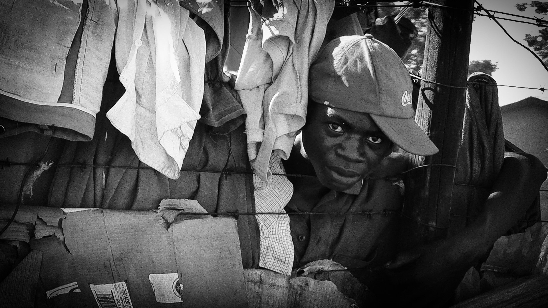 A Zimbabwean refugee youth looks through a barbedwire fence surrounded by his posessions.