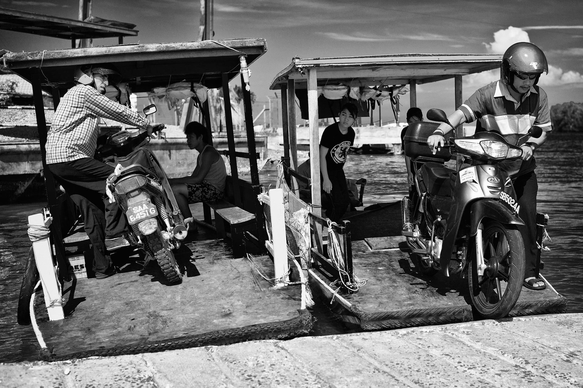 Two small ferries shuttle riders and their motorcycles across a waterway in Sabah, Malaysia.