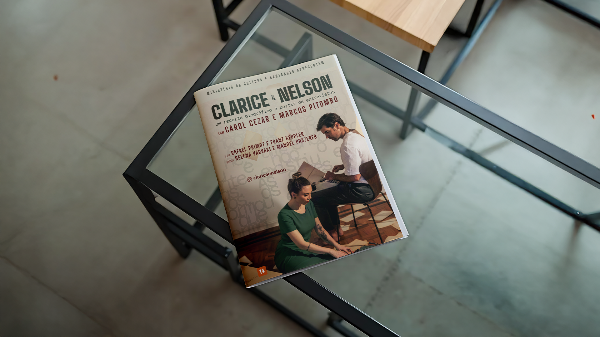 Mockup do programa impresso da peça 'Clarice & Nelson' repousando sobre uma mesa de vidro moderna. A capa destaca o título, os nomes do elenco Carol Cezar e Marcos Pitombo, e uma fotografia central dos atores em cena, envoltos por uma textura tipográfica suave ao fundo.