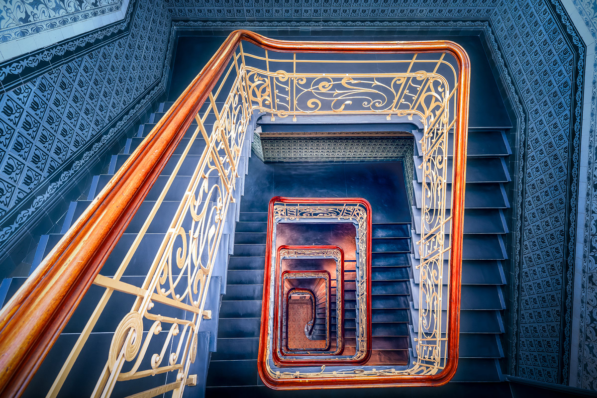 Nicole Holz - Fine Art Editions |  Holstenhof Hamburg | Architektonische Fotokunst des expressionistischen Treppenhauses. Der Blick folgt den geschwungenen, monumentalen Linien und der sakralen Schwerkraft historischer Kontorhaus-Architektur in einem präzisen Zusammenspiel von Licht und Schatten.  Architectural fine art photography of an expressionist staircase. The composition captures the sweeping, monumental lines and sacred gravity of historic corporate architecture through a precise interplay of light and shadow.
