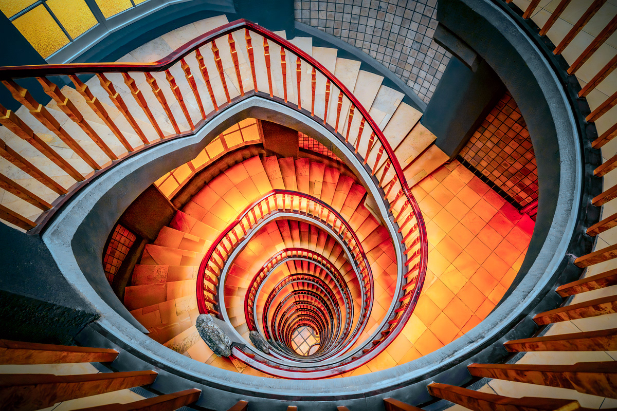 Nicole Holz - Fine Art Editions |  Messberghof Hamburg | Architektonische Fotokunst des expressionistischen Treppenhauses. Der Blick folgt den geschwungenen, monumentalen Linien und der sakralen Schwerkraft historischer Kontorhaus-Architektur in einem präzisen Zusammenspiel von Licht und Schatten.  Architectural fine art photography of an expressionist staircase. The composition captures the sweeping, monumental lines and sacred gravity of historic corporate architecture through a precise interplay of light and shadow.