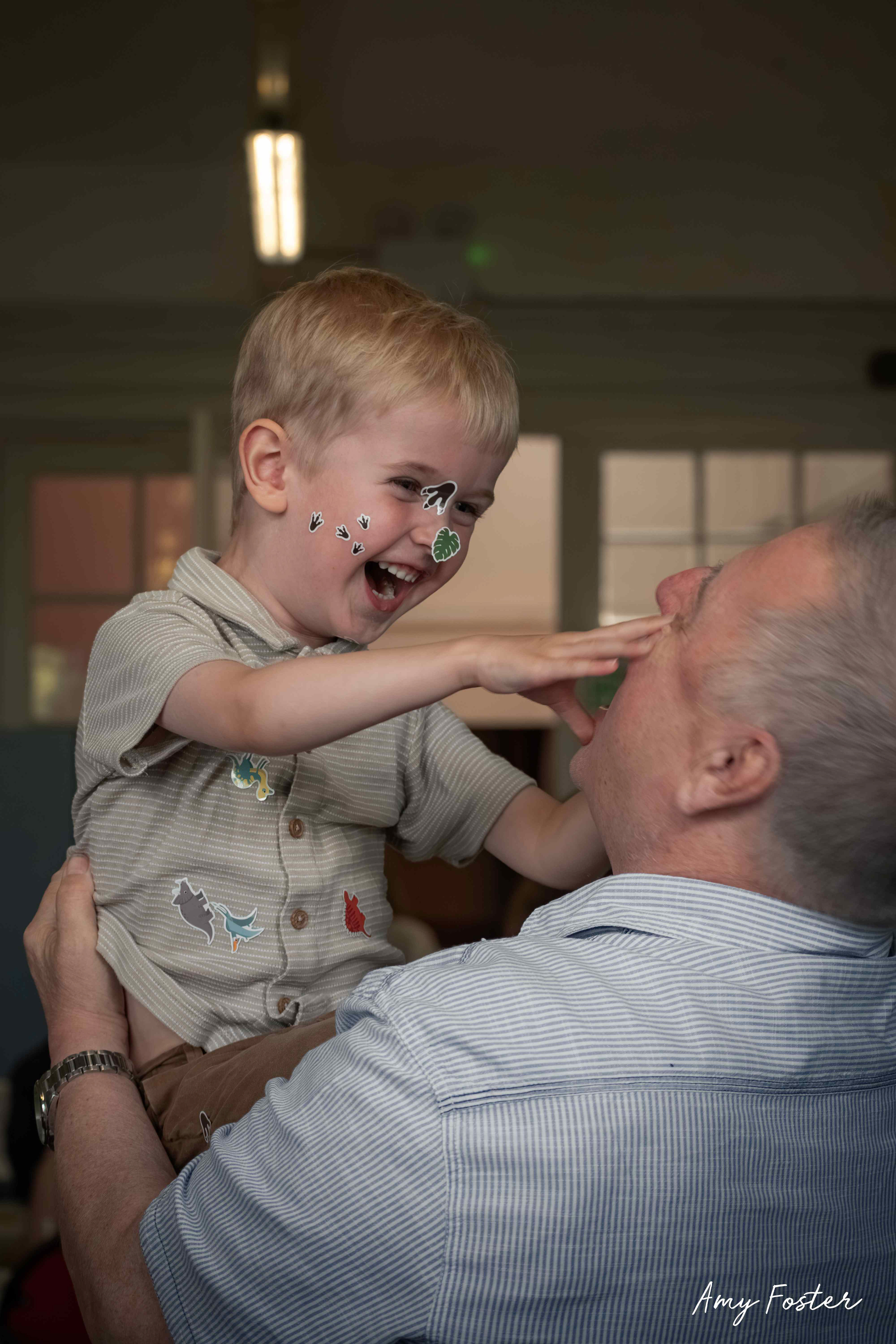 Young child with a face covered in fun stickers smiling in the arms of grandparent 
