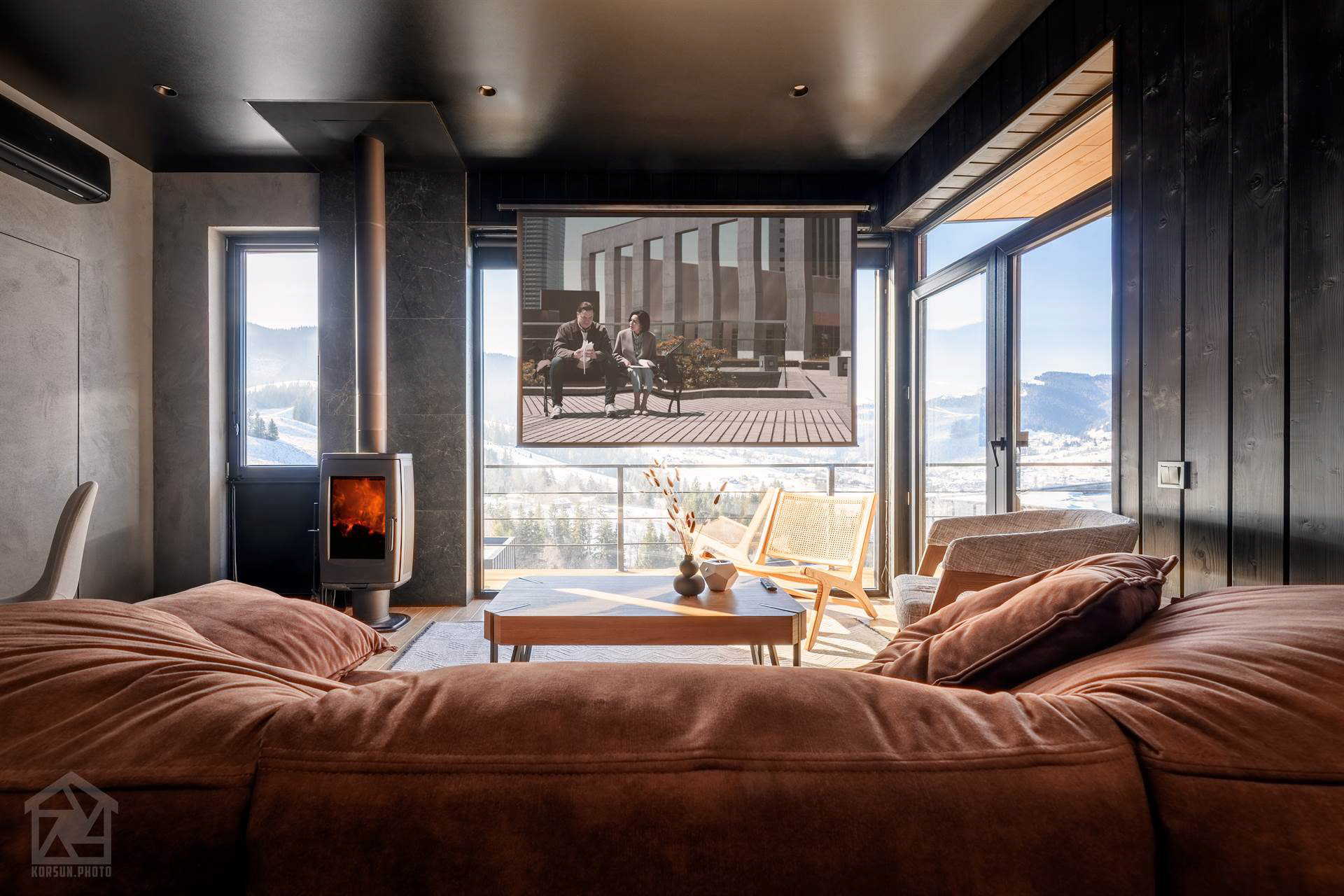 Проєктор та екран у зоні відпочинку замість традиційного телевізора в одному плані з каміном з живим полум’ям