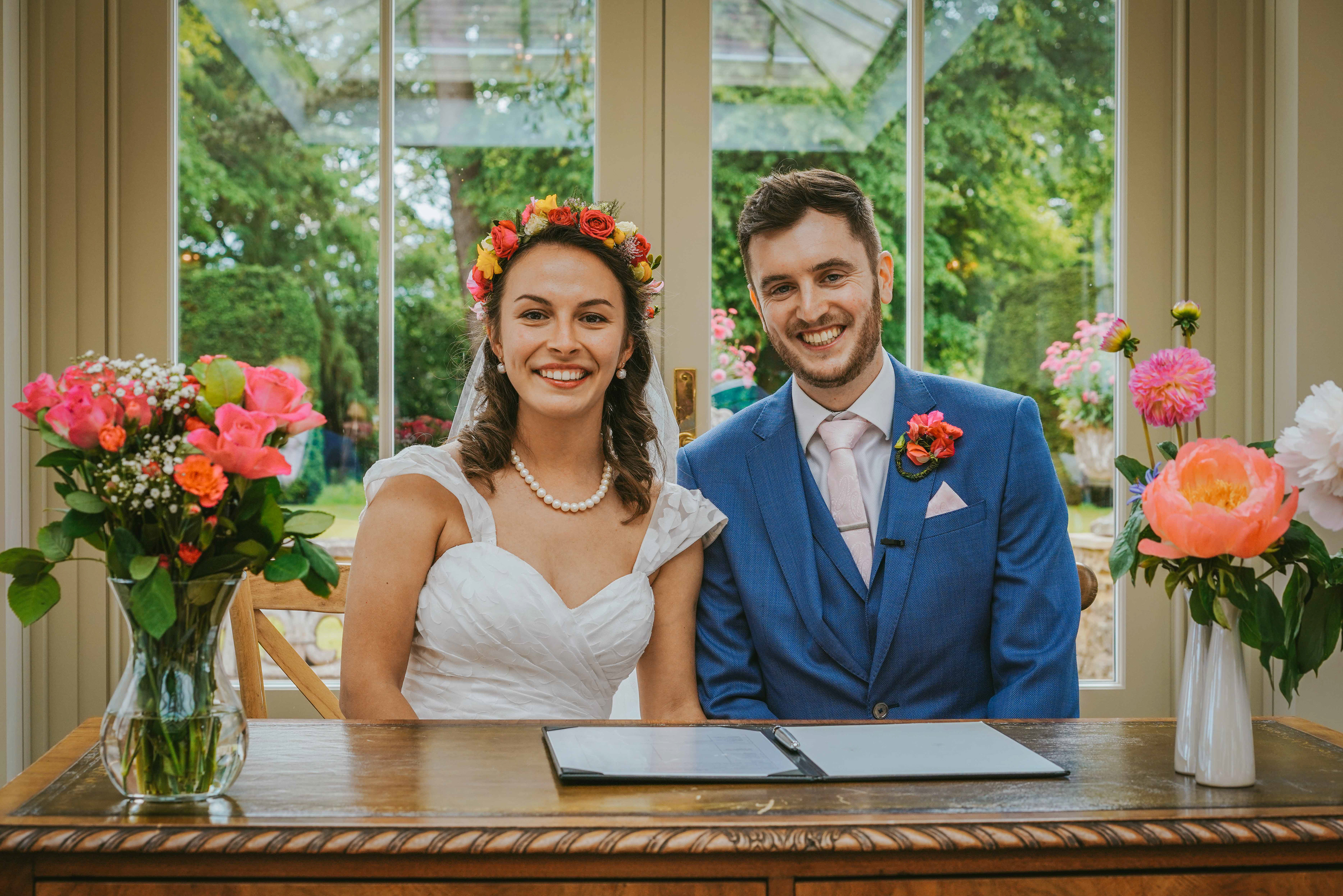 bride and groom stephen and gaydeliya smiling at buckinghamshire wedding photographer david lefebvre surrounded by pink and white flowers at an oak table