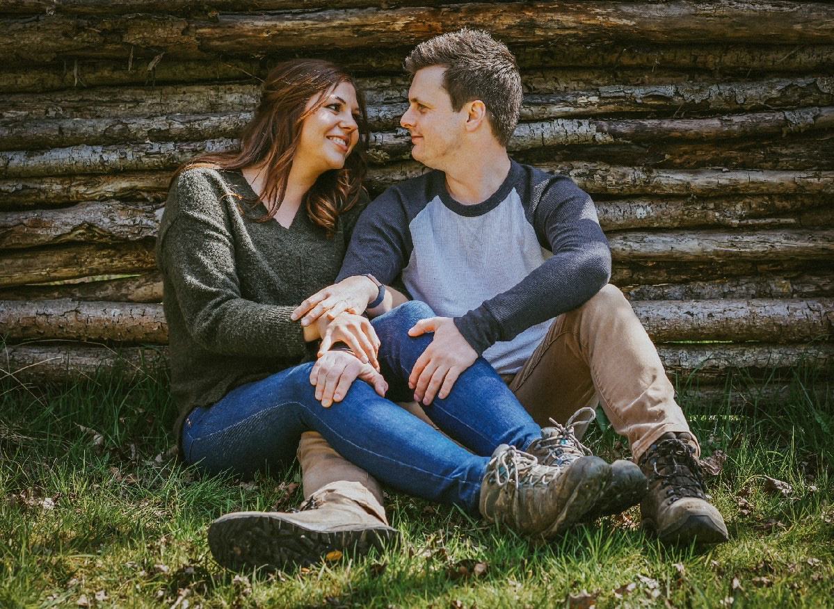 engaged pair sat against wooden wall outside in the sun at endeavour woodland wedding venue in swanbourne with british wedding photographer david lefebvre from buckingham