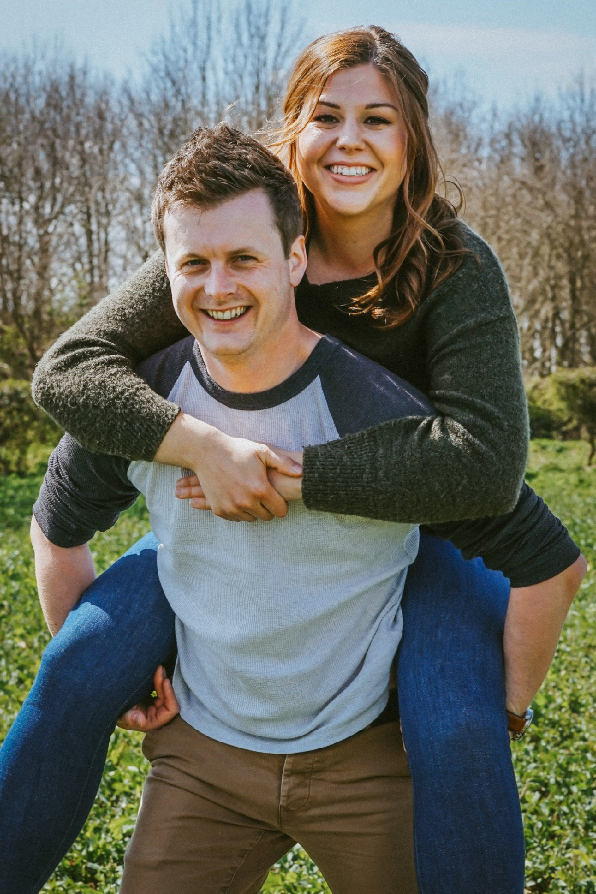 close up of couple smiling at camera on piggy back in rapeseed field in swanbourne uk in pre wedding engagement shoot with david lefebvre a wedding photographer from buckinghamshire covering milton keynes and oxfordshire