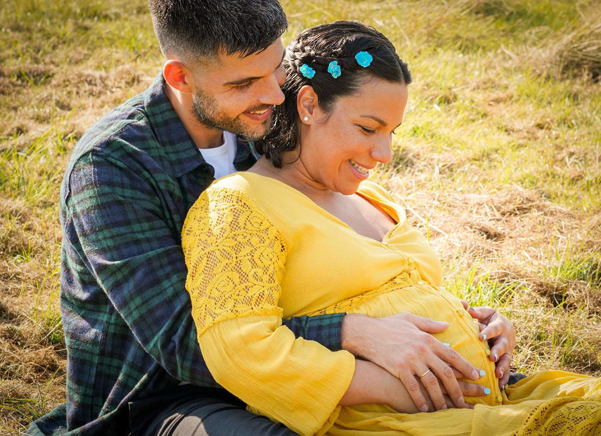 close up of romantic greek and italian couple sat together in long grass by lake in the summer at claydon house near steeple claydon in buckinghamshire on a candid mini maternity photo shoot session