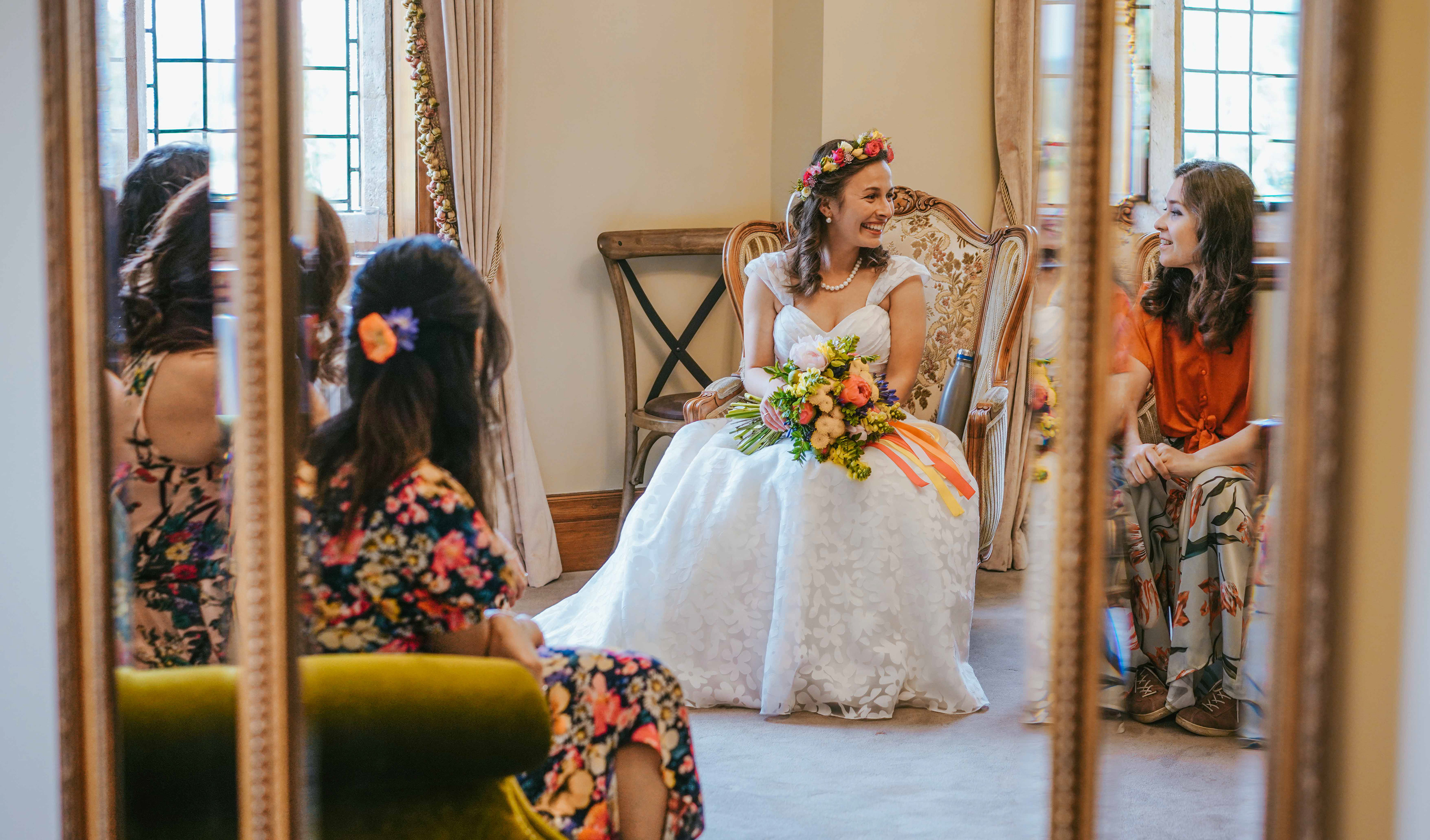 bride gaydeliya sat with bridesmaids looking at her white dress in mirror reflection smiling with maid of honour at towcester wedding at plum park manor by david lefebvre photography