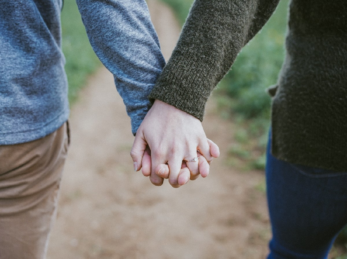 close up of couple walking away hand in hand wearing rings at rapeseed field in swanbourne uk on pre wedding engagement photo shoot session with wedding photographer david lefebvre
