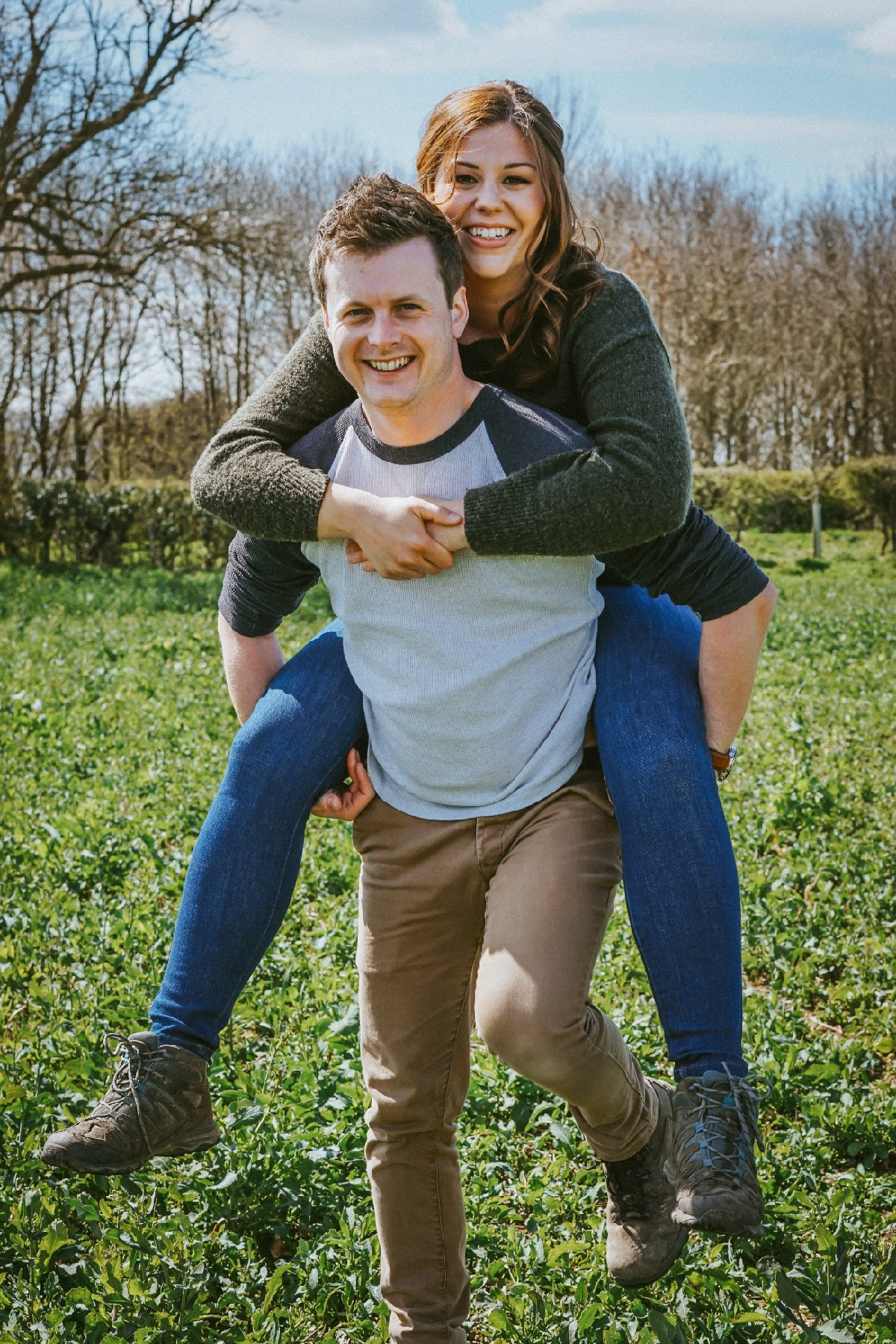 couple smiling at camera on piggy back in rapeseed field in swanbourne uk with david lefebvre a wedding photographer from buckinghamshire covering milton keynes and oxfordshire