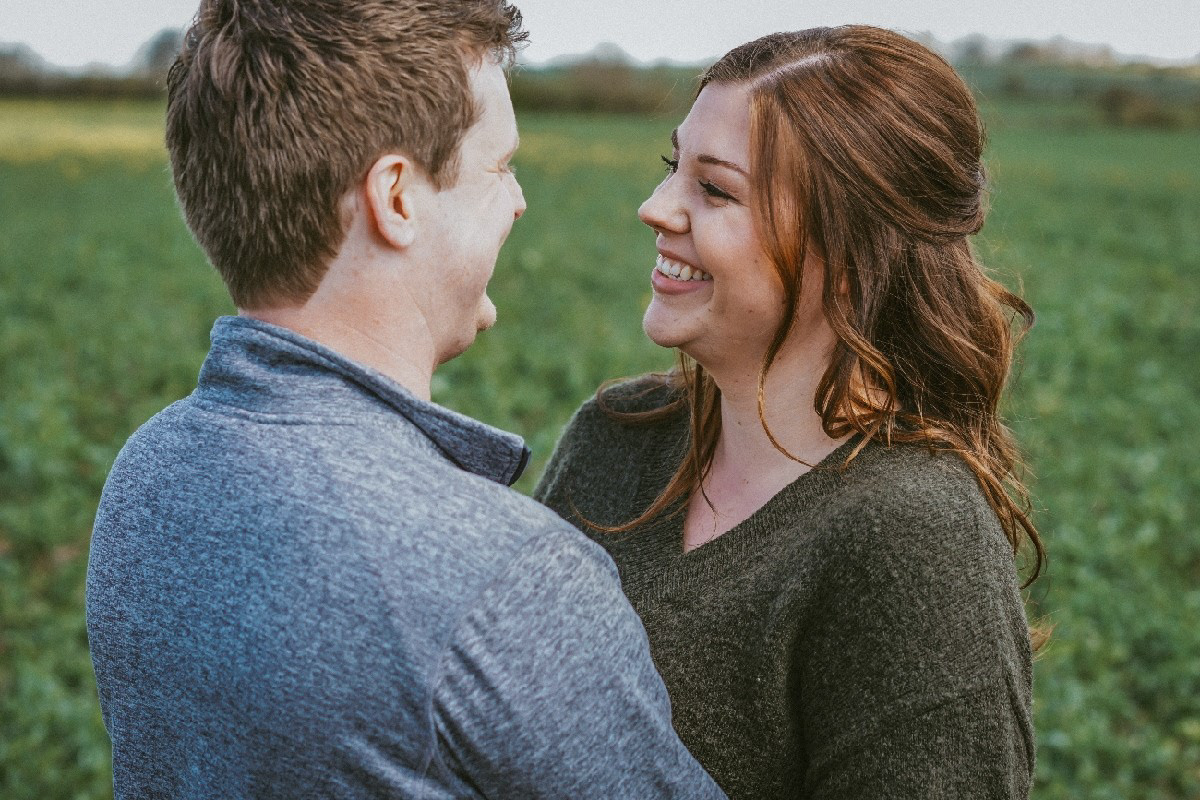couple laughing together arm in arm candidly in rapeseed field near swanbourne in buckinghamshire during a pre wedding engagement photo shoot session with david lefebvre from milton keynes