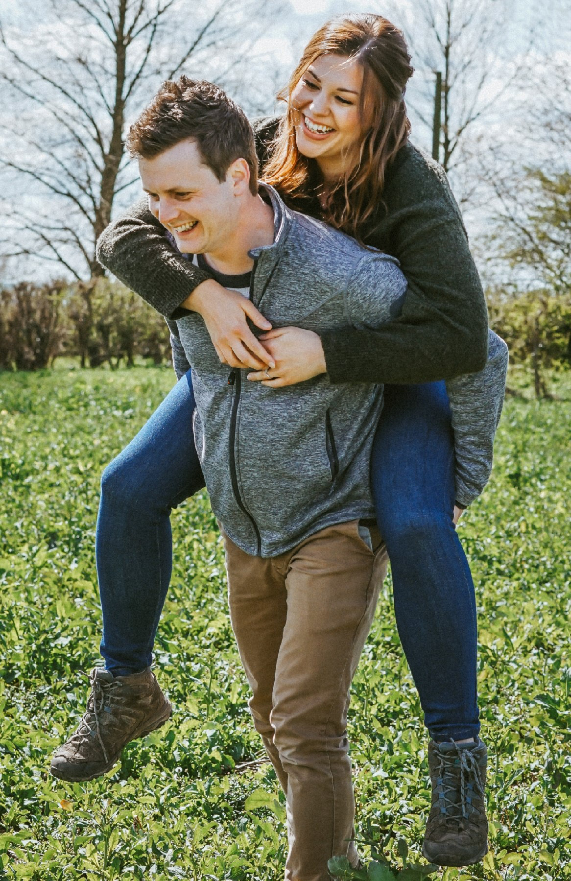 smiling laughing couple enjoying piggy back ride in rapeseed field in swanbourne during pre wedding engagement shoot with warm colours and big smiles