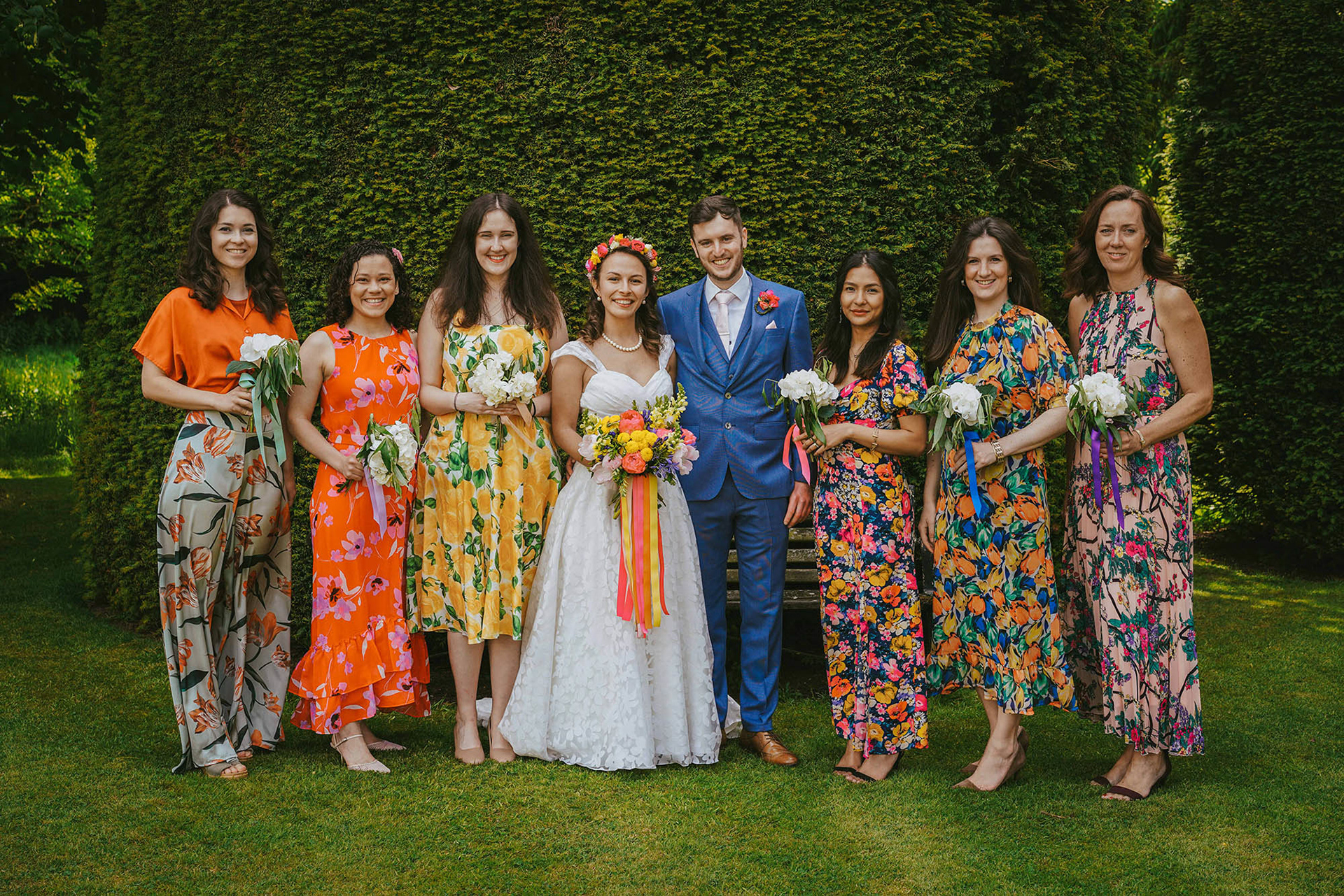 vibrantly dressed guests stand on grass smiling at colourful wedding in towcester at plum park hotel venue featuring bride and groom taken by photographer david lefebvre photography