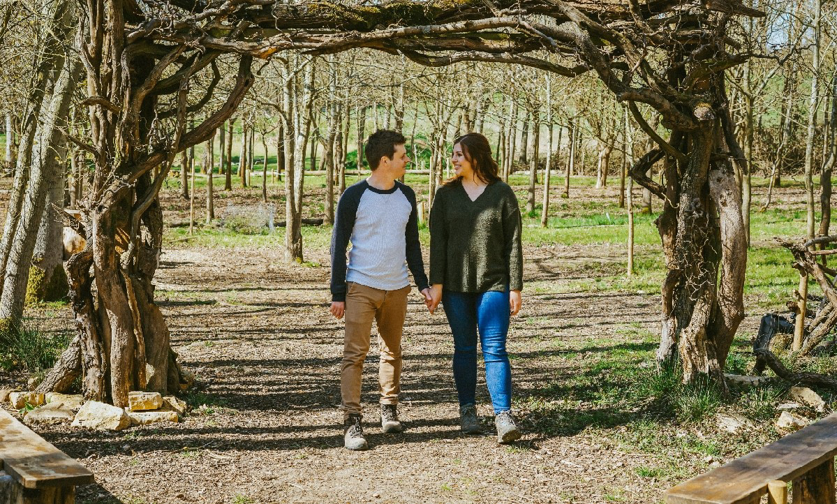 soon to be bride and groom stood during pre wedding engagement shoot with david lefebvre wedding arch made of tree branches in spring