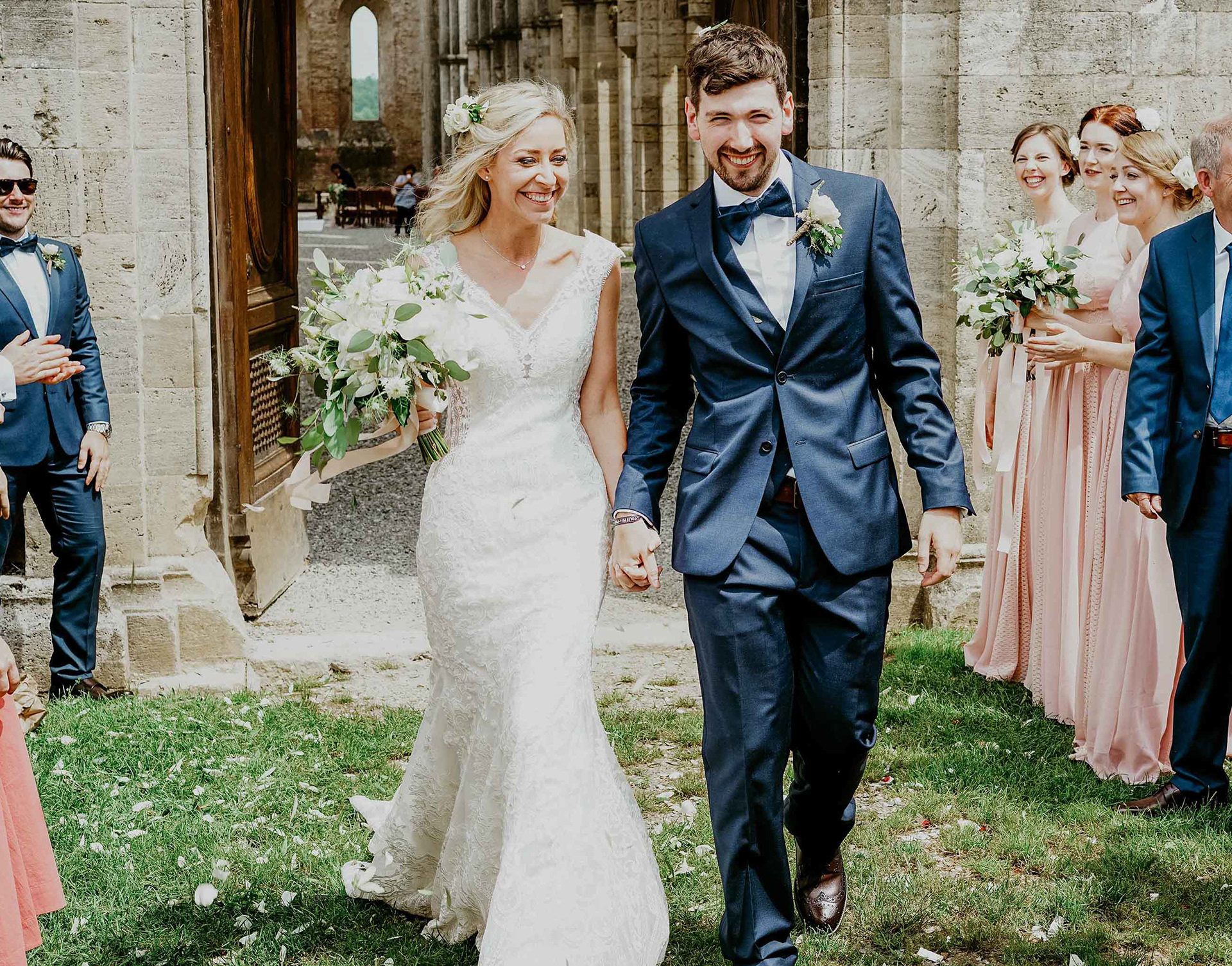 smiling bride and groom leaving san galgano abbey in italy