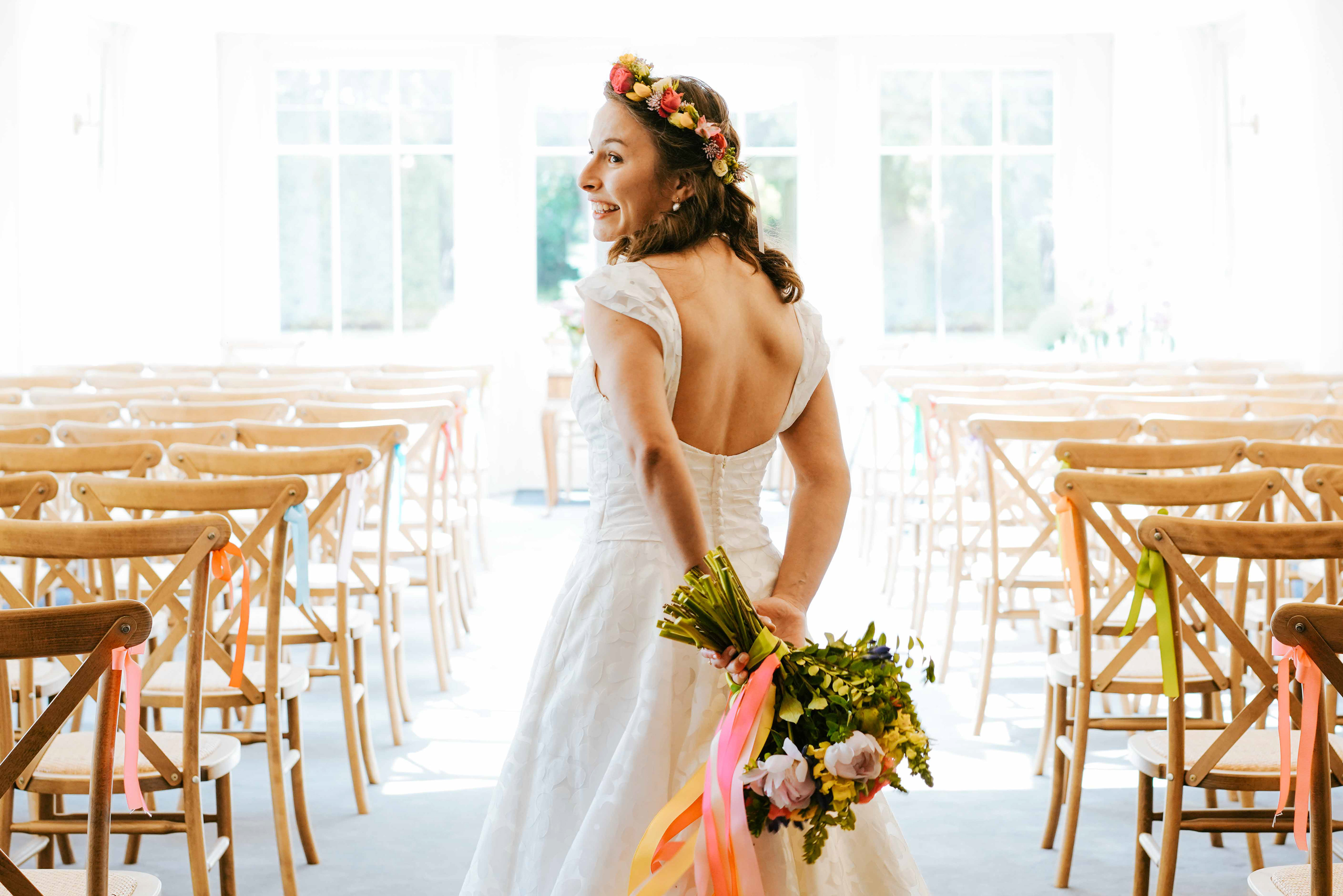 beautiful tanned bride stood holding floral bouquet wearing headband and pearl earrings by wooden seats at aisle at plum park manor taken by wedding photographer david lefebvre