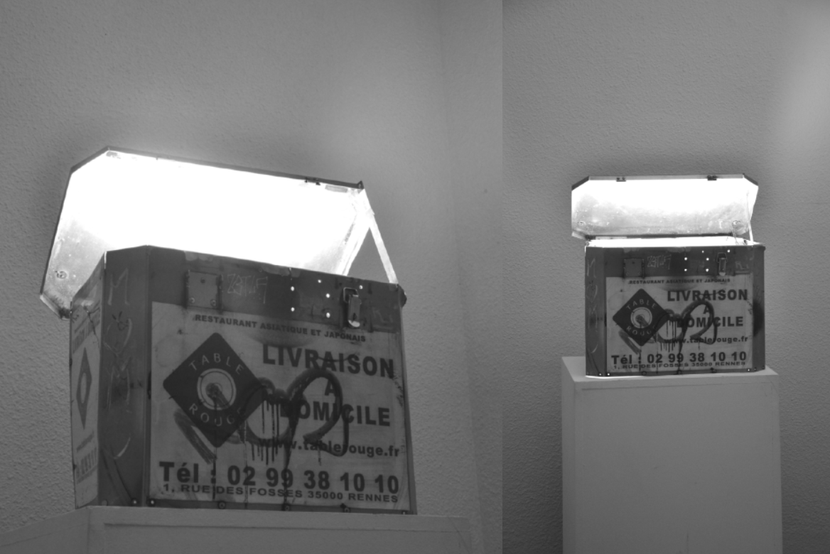 Exposition HUbert, Galerie Awen, Rennes, Fossile de l’ère pré-uberienne, installation, 2023. Caisse métallique sur cimaise, avec une lumière jaillissant et présentée dans une petite pièce sombre. Une caisse métallique abandonnée par un restaurant, aux couleurs de celui-ci, est exposée comme un fossile. Elle rappelle une époque où la gestion des livraisons étaient à la charge des restaurants. L'installation montre ainsi l'impact de l'ubérisation sur les entreprises de restauration, tout en créant une mise en scène qui révèle un trésor caché à l'intérieur de la boîte. © Elsa Tessier
