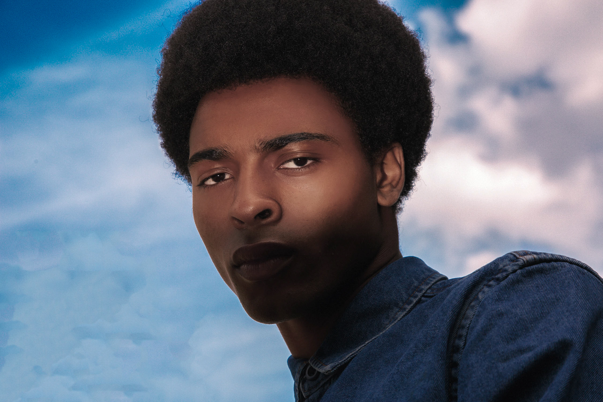 A stunning background of  a blue sky with a male model in the frame wearing blue denim for a fashion porject