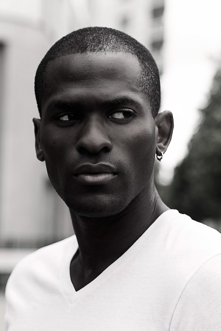 black and white image of a male model in white v neck top with his eyes locked into something to his left