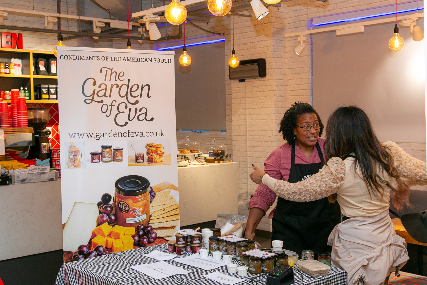 A lady at her stand with products on a table and a banner with her branding for an event spill the beans 