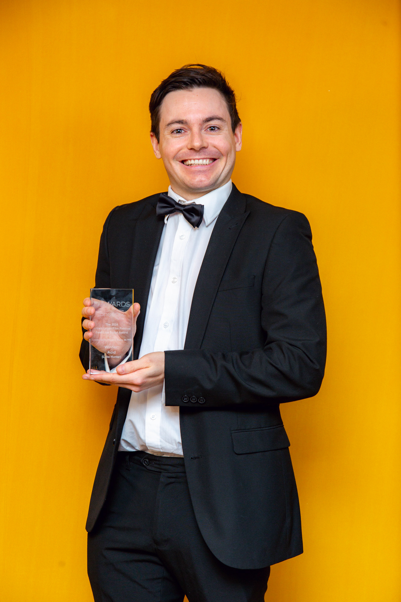 Winner with a bigh grin wearing a black tux and bowtie with his award -  BUFF AWARDS 2024