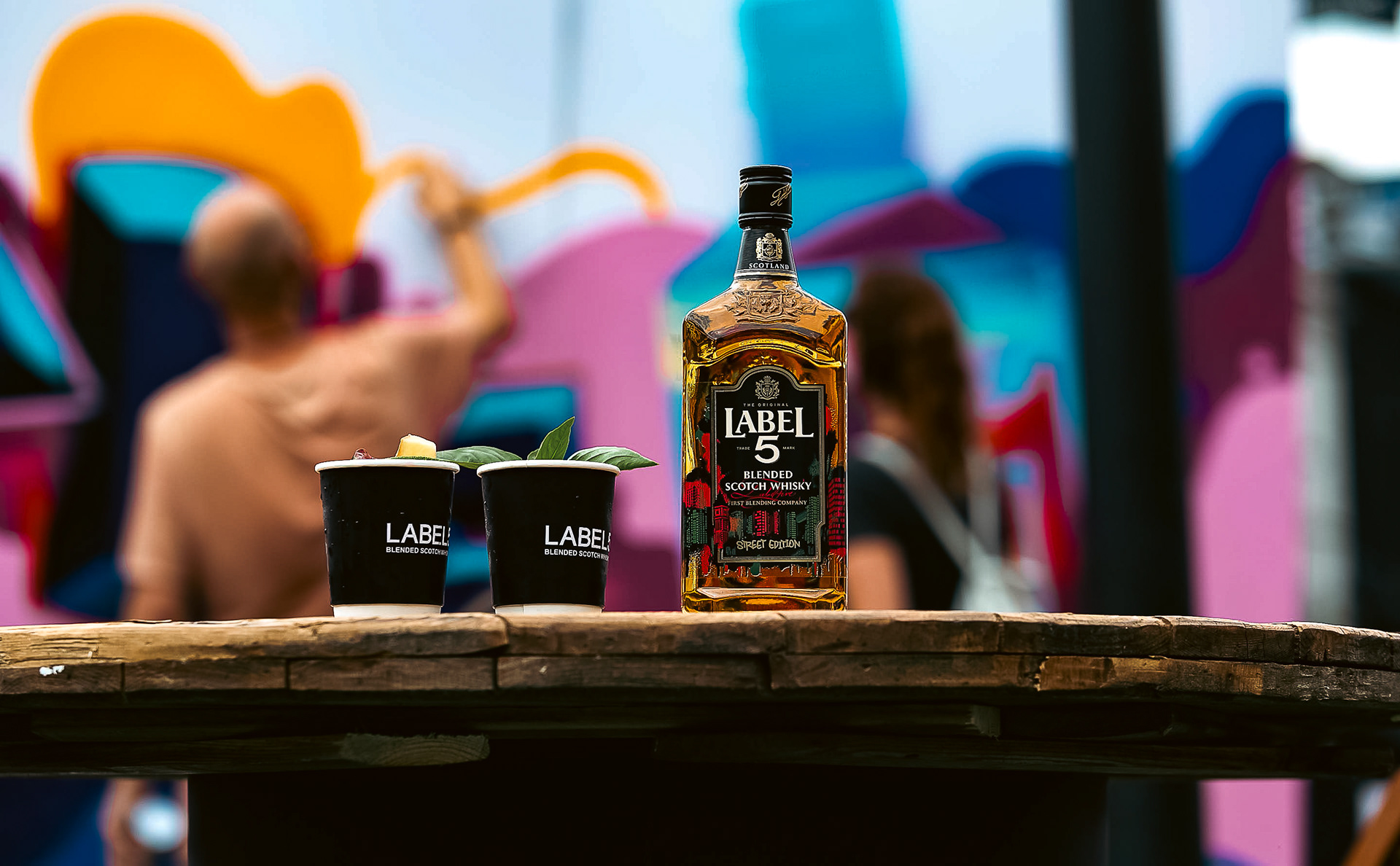 Label 5 bottle on a table with two plastic cups filled with drink next to it 