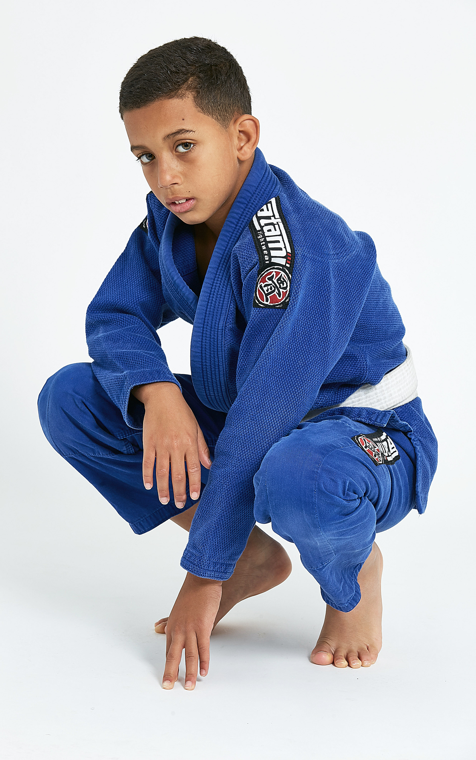 young boy in blue karate uniform in a squat position, taken in a studio with white backgrounds