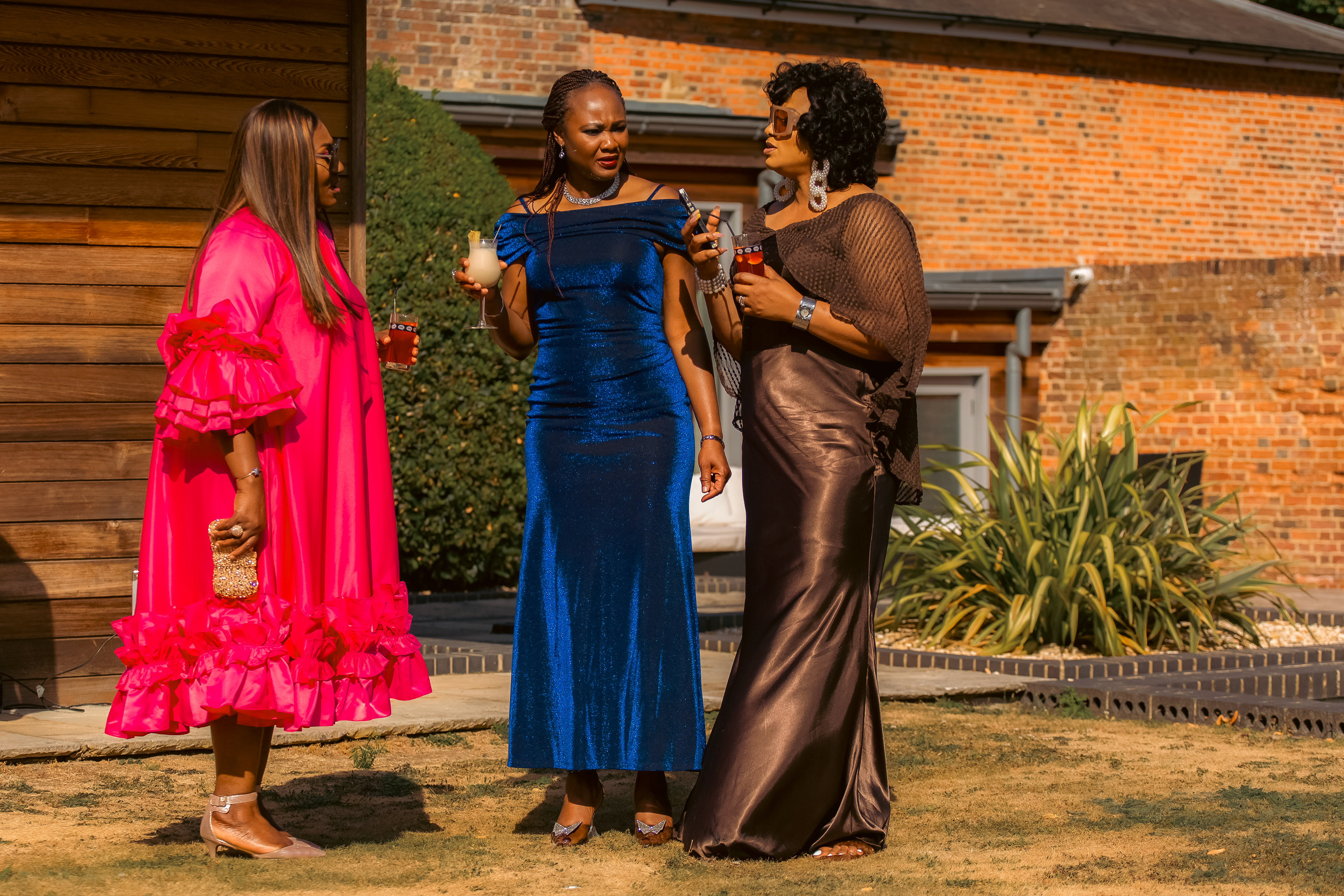 Three ladies in pink, blue and brown dresses having a drink and waiting for the event to begin