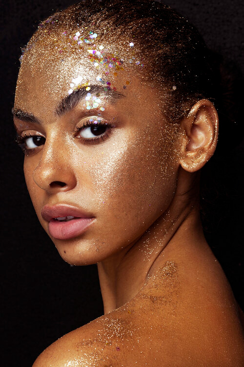 glitter and gold beauty project with model looking back over shoulder with a well lit face and black background
