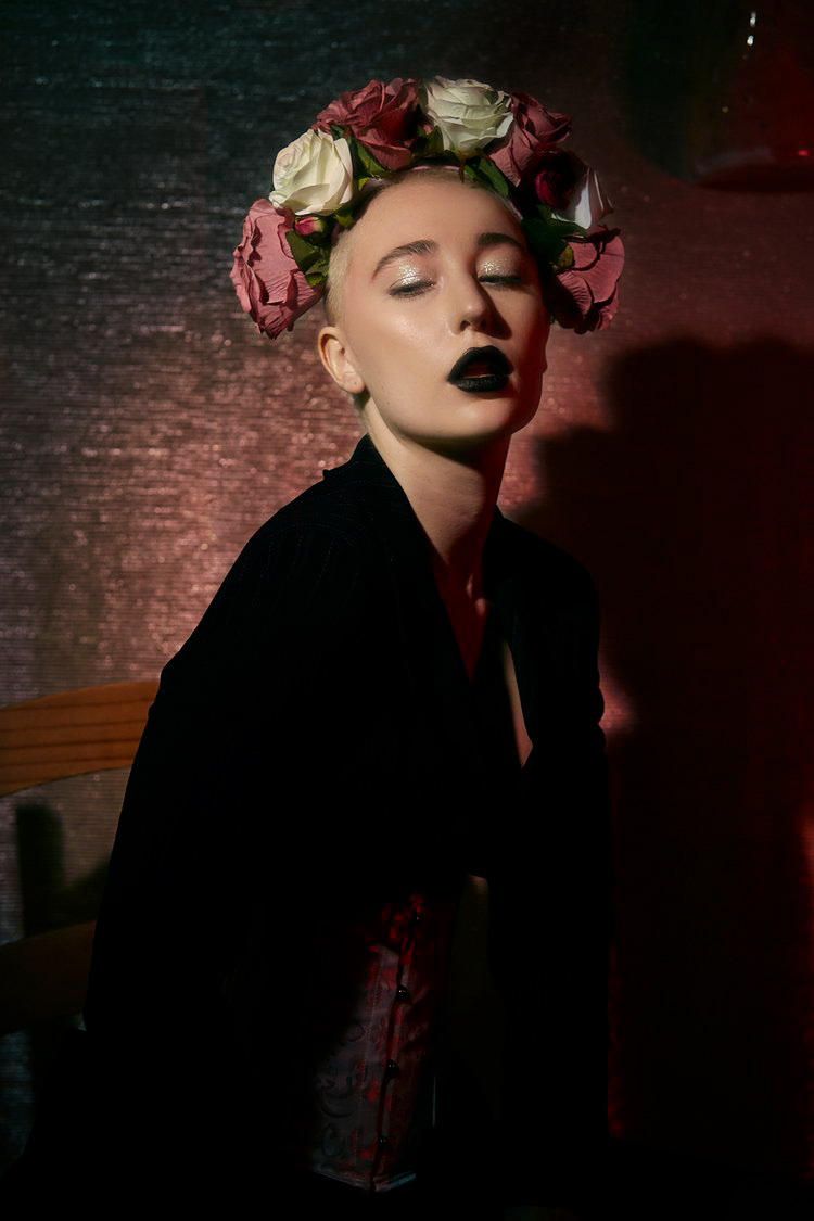 Creatively lit model in front of a dark background with a flower crown on her head