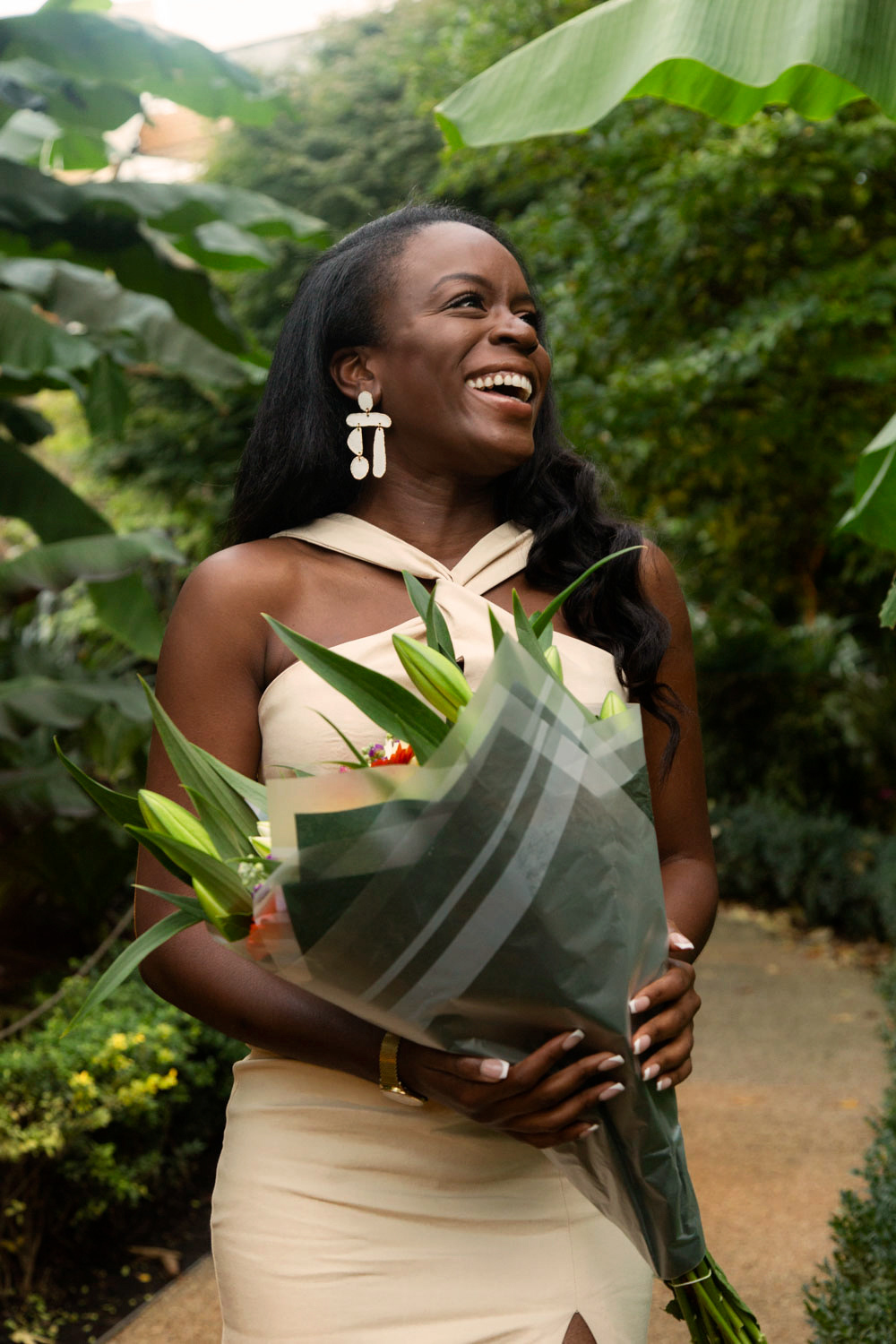 Happy and Newly engaged, woman holding flowers in a forest like setting holding flowers with a big smile on her face 