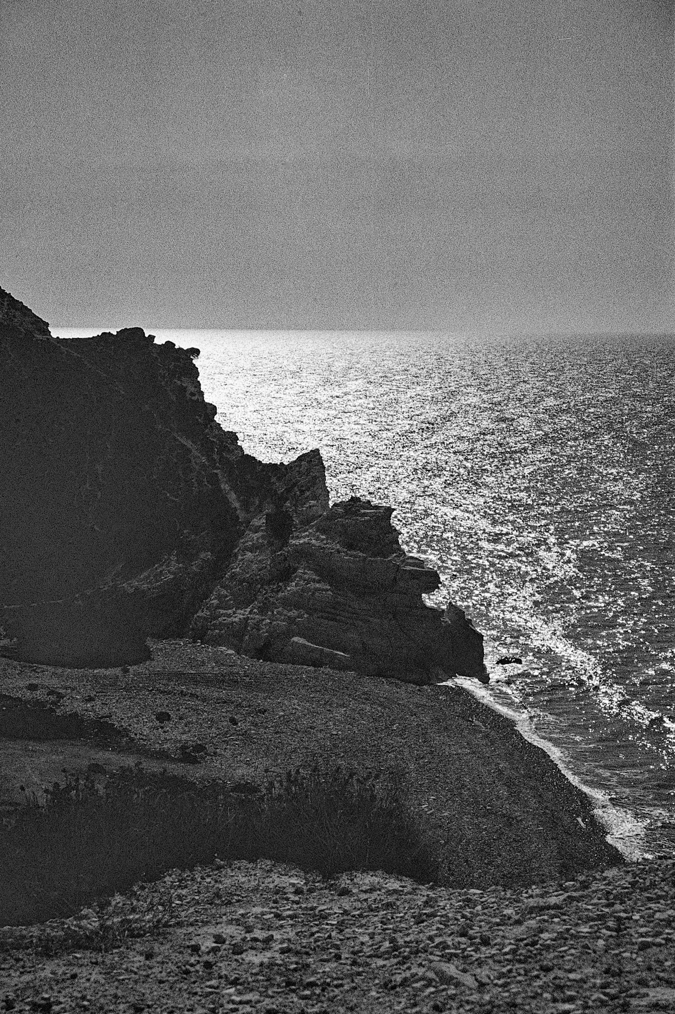 Wind and sea carve a rugged limestone cliff as light scatters across the shimmering Mediterranean below.