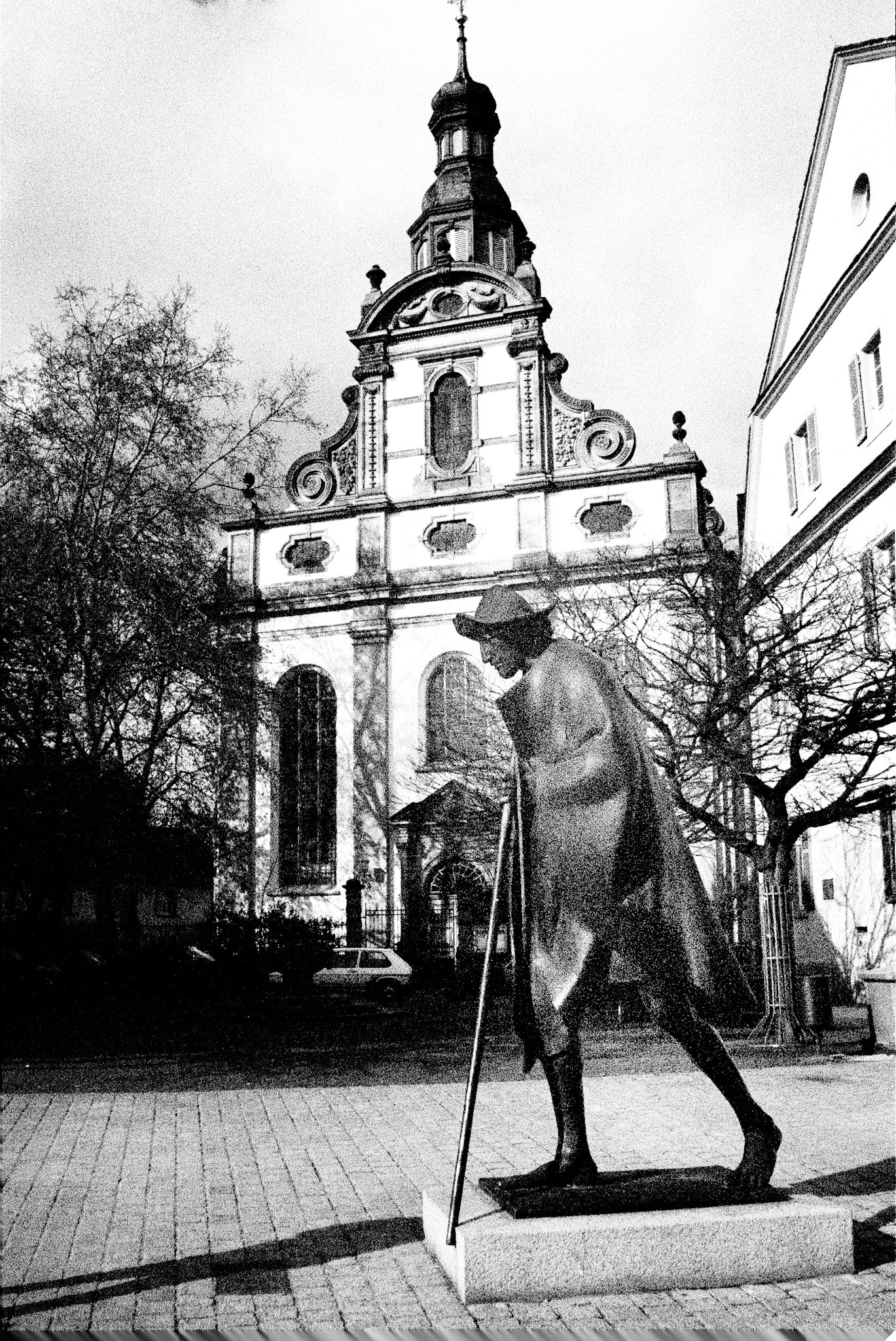 Der Spaziergänger, The Walker, Heidelberg .  A solitary bronze figure strides across the square before Heidelberg’s Jesuit Church, bridging modern sculpture and Baroque architecture.