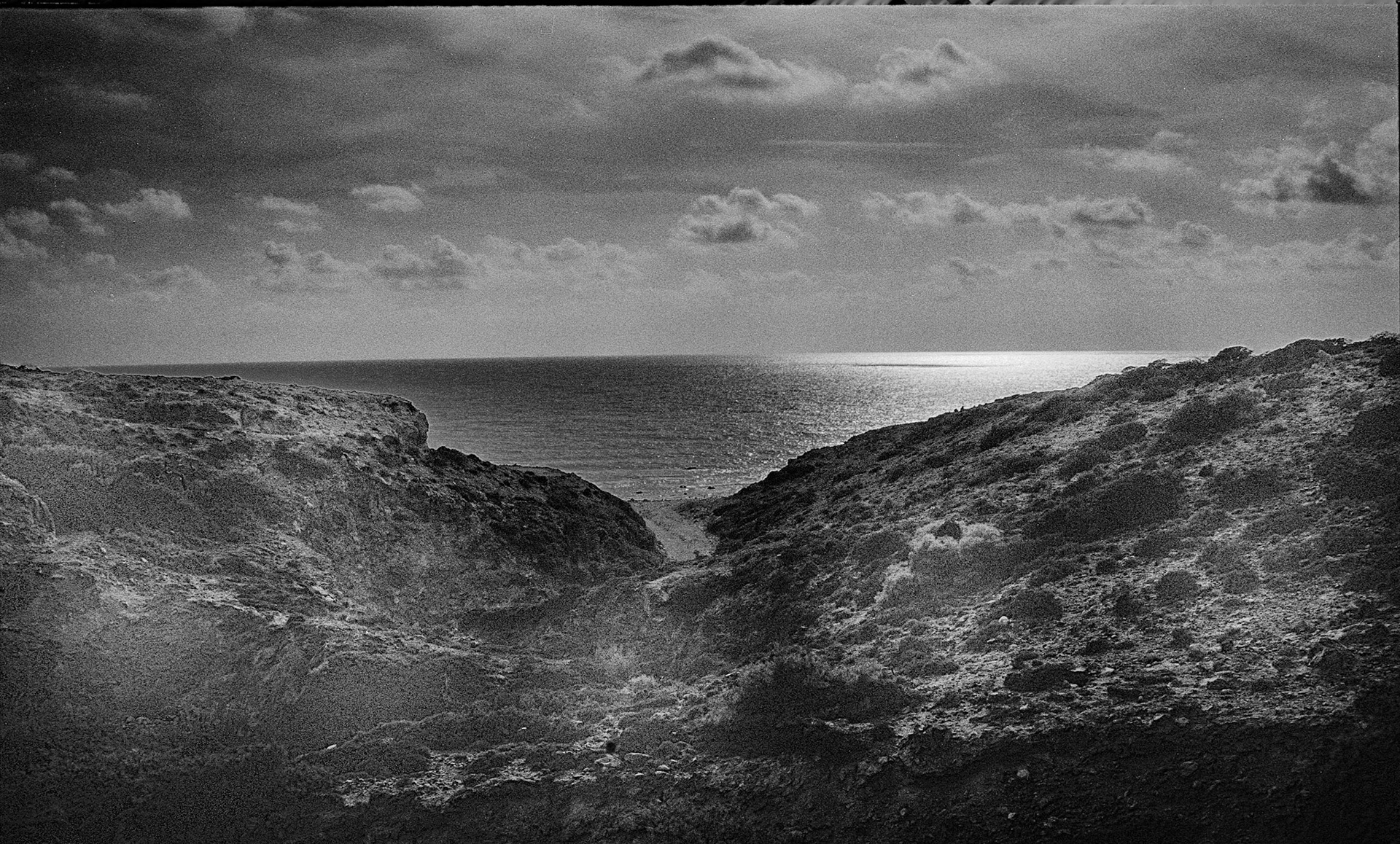 A narrow rocky valley opens toward a shimmering horizon, guiding the eye from shadow into light.
