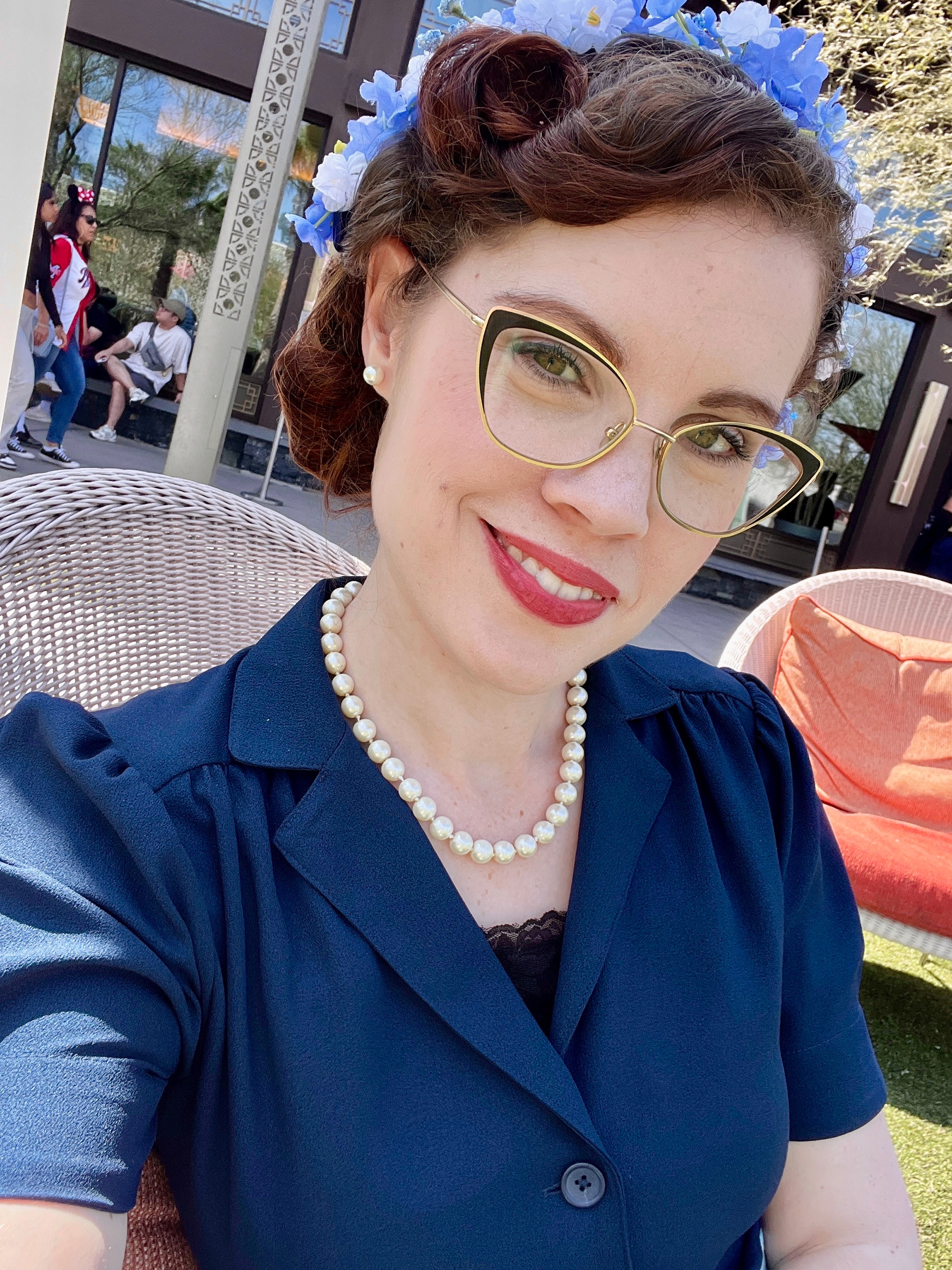 Picture of Kaytie dressed in her 1950's styled outfit Disney bounding as the Disneyland Hotel. Kaytie is also wearing cat eyed glasses and a handmade vintage styled hat with blue and white flowers.