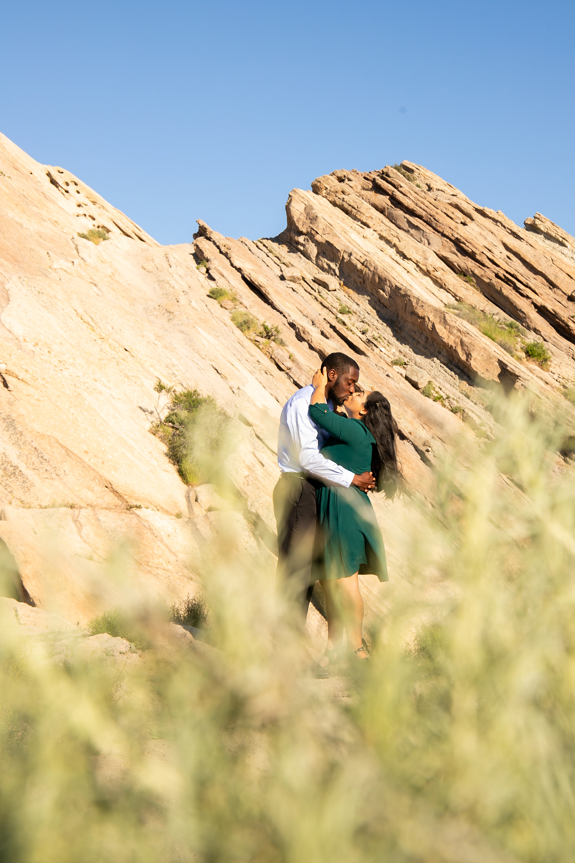 A couple exchange a loving kiss with a rocky peak background.