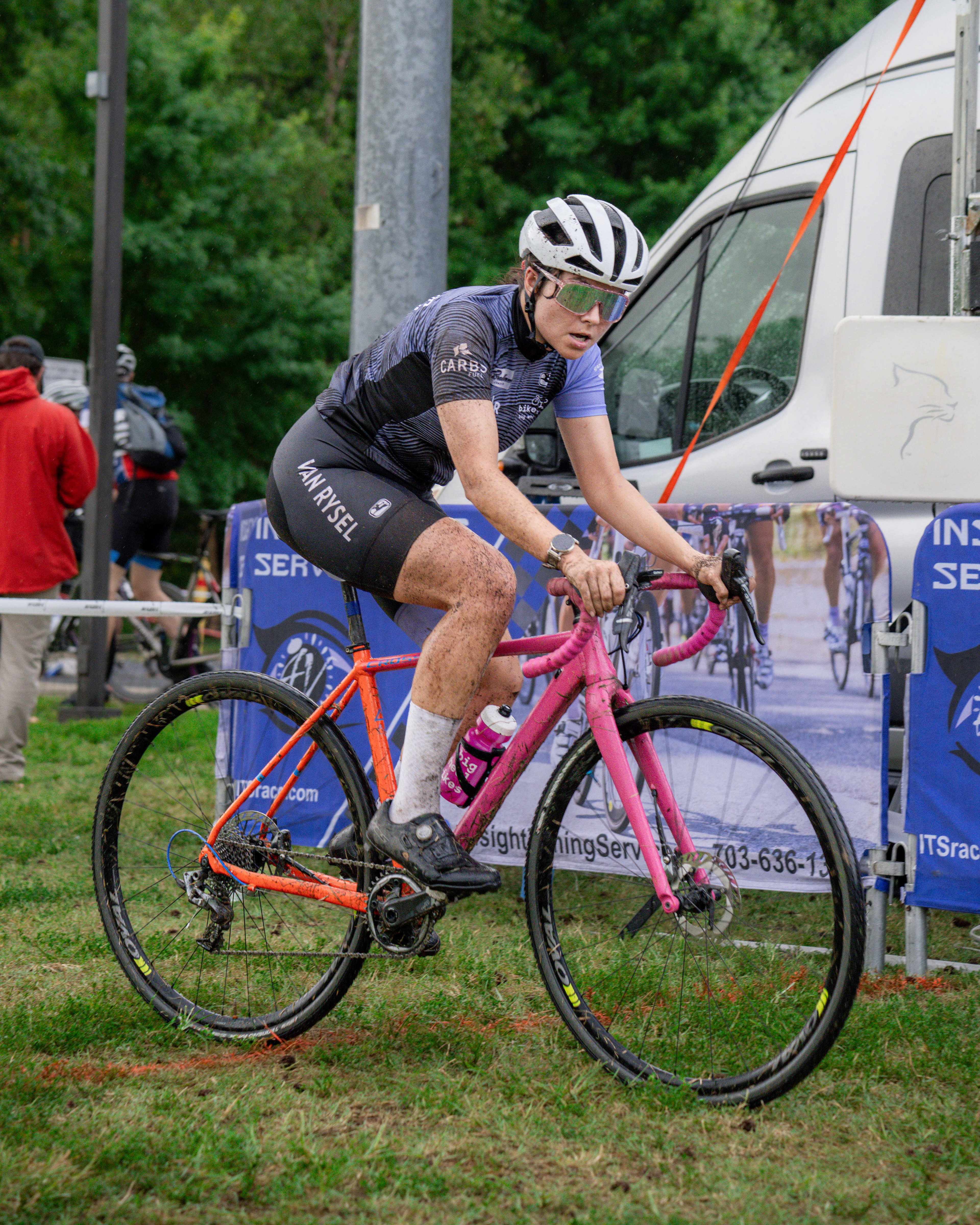 A woman on a pink and orange bicycle covered in mud.