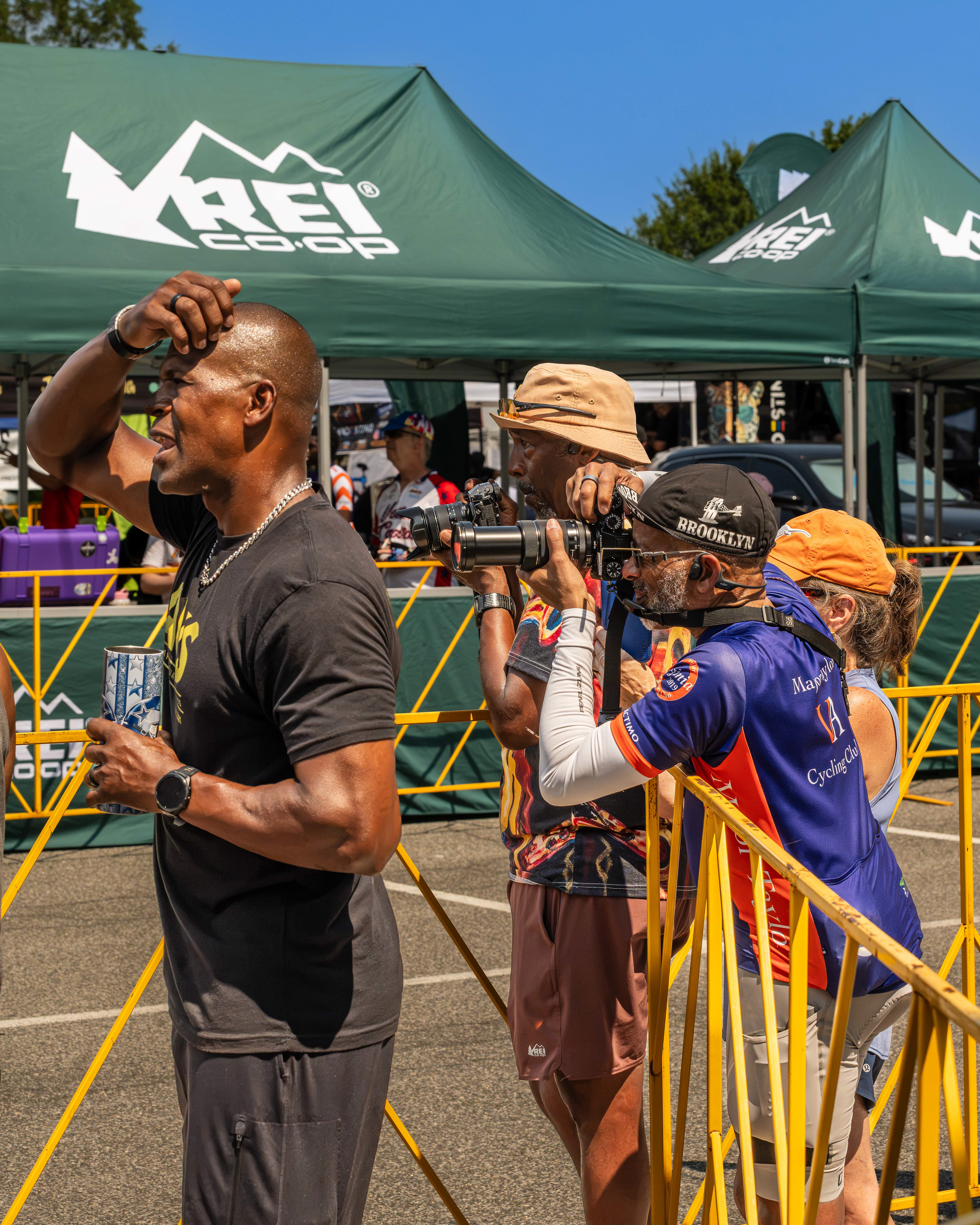 Three men watching a bike race, two of whom have cameras.