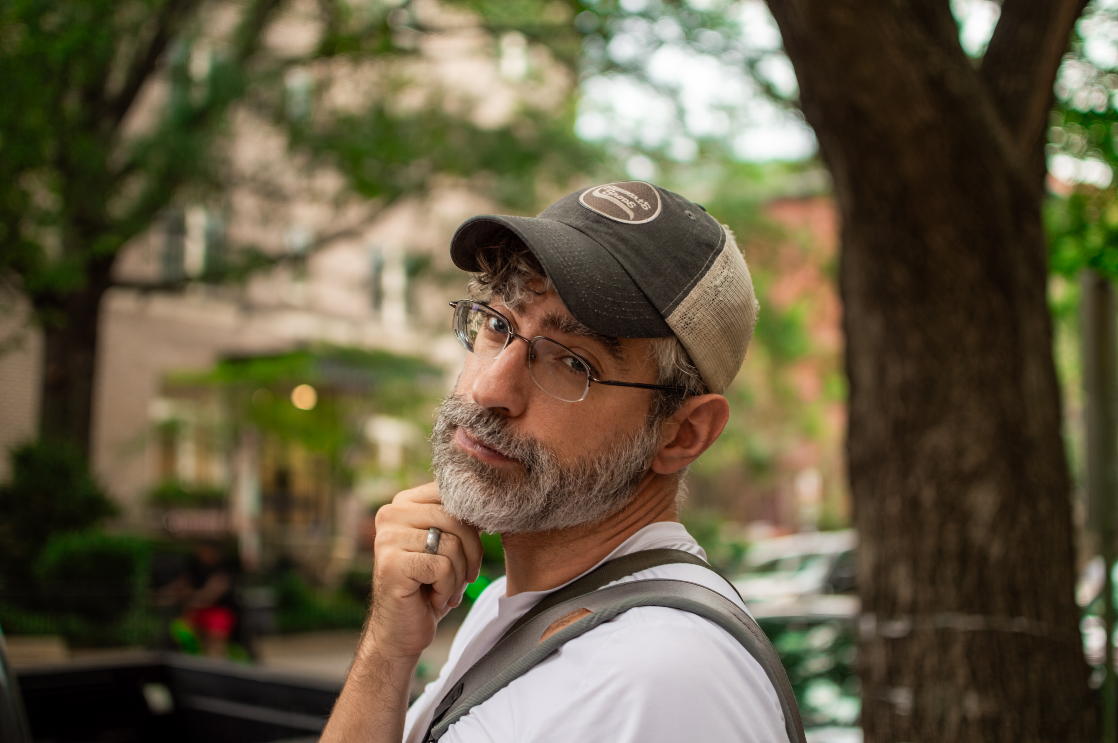A photo of a white man in his early 40s with a beard, glasses, and a baseball hat smiling at the camera.