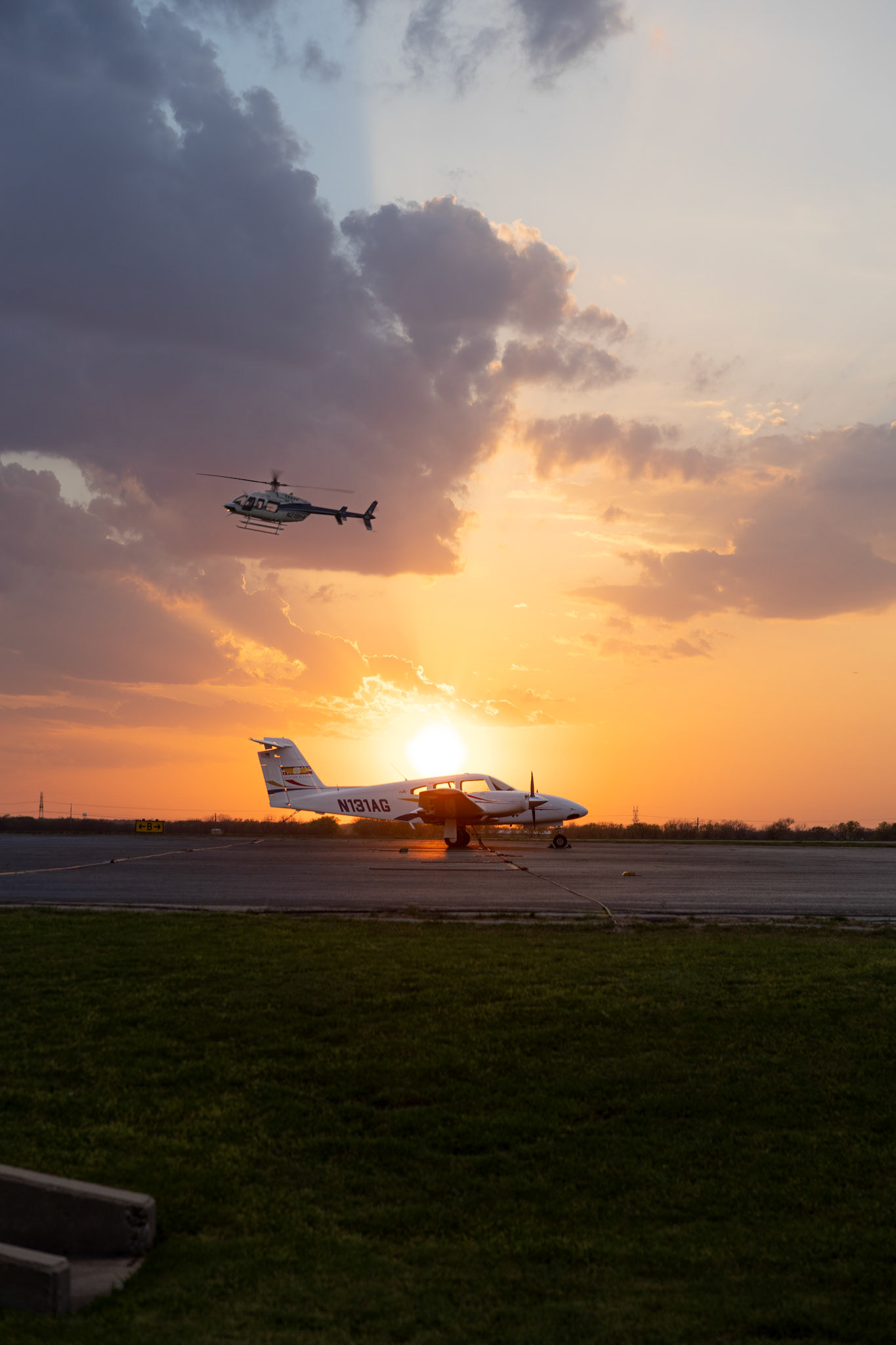  WINGS OF FREEDOM- A helicopter glides above a PA 44 Seminole plane at the Denton US Aviation Academy, March 25, 2025 Tuesday night. The PA 44 Seminole awaits its next pilot to take it into flight.  Photo by Alaina Jones 