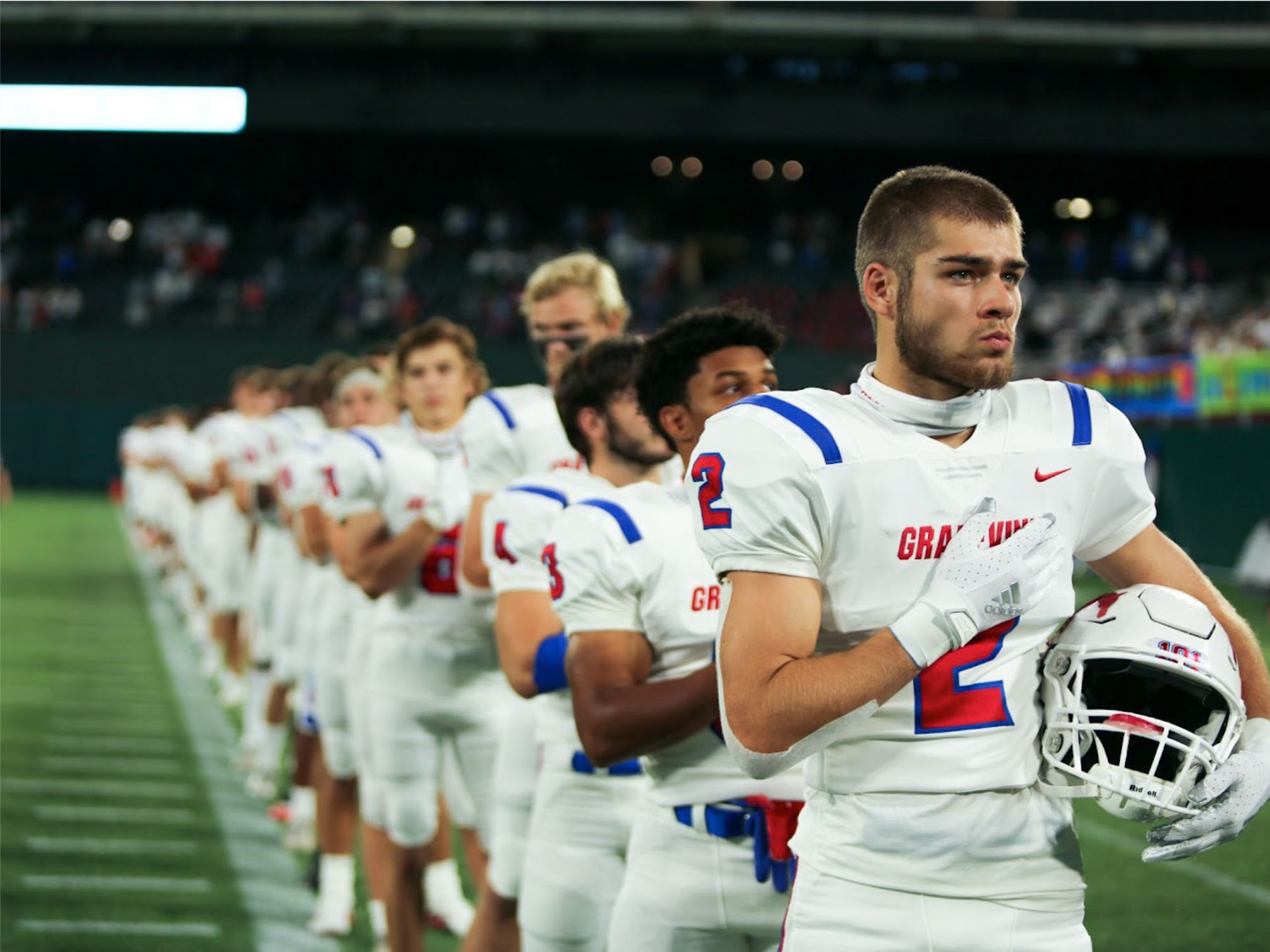 HONOR- Moments before kickoff at the annual Battle of the Red Rail rivalry game, Grapevine High School football players stand in honor of the national anthem at Mustang-Panther Stadium, facing off against Colleyville Heritage. By Alaina Jones