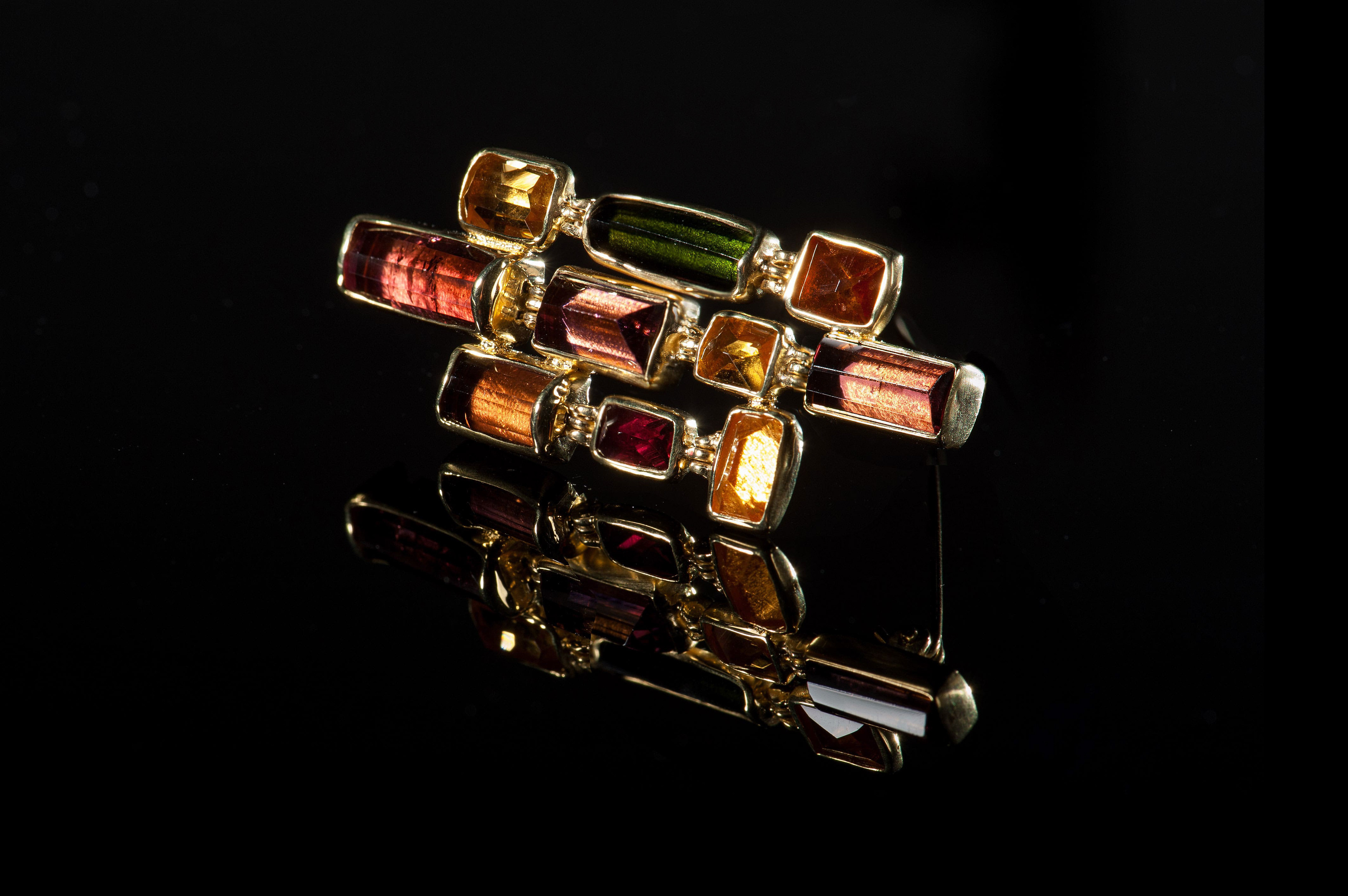 Margoni jewellery: καρφίτσα χρυσή σε ακανόνιστο σχέδιο με διαφορετικούς ημιπολύτιμους λίθους σε αποχρώσεις κόκκινου και καφέ