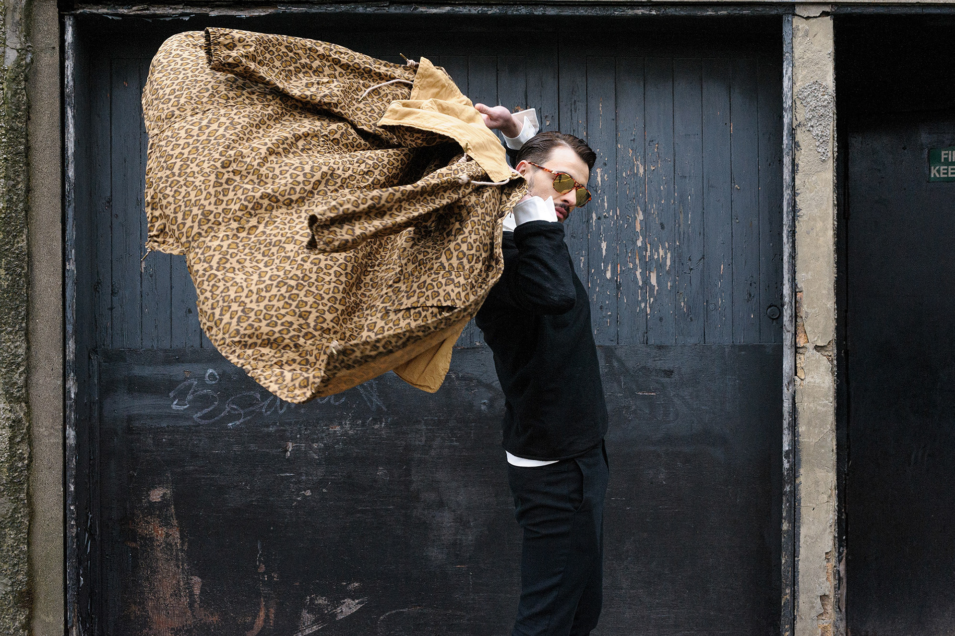 Άνδρας σε αστικό περιβάλλον, καθώς ρίχνει πίσω το παλτό του με δυναμική κίνηση. Φωτογράφιση μόδας με φυσικό φως και μινιμαλιστική αισθητική.,      Man in an urban setting tossing his coat back in motion. Fashion photography with natural light and minimalist aesthetics.   