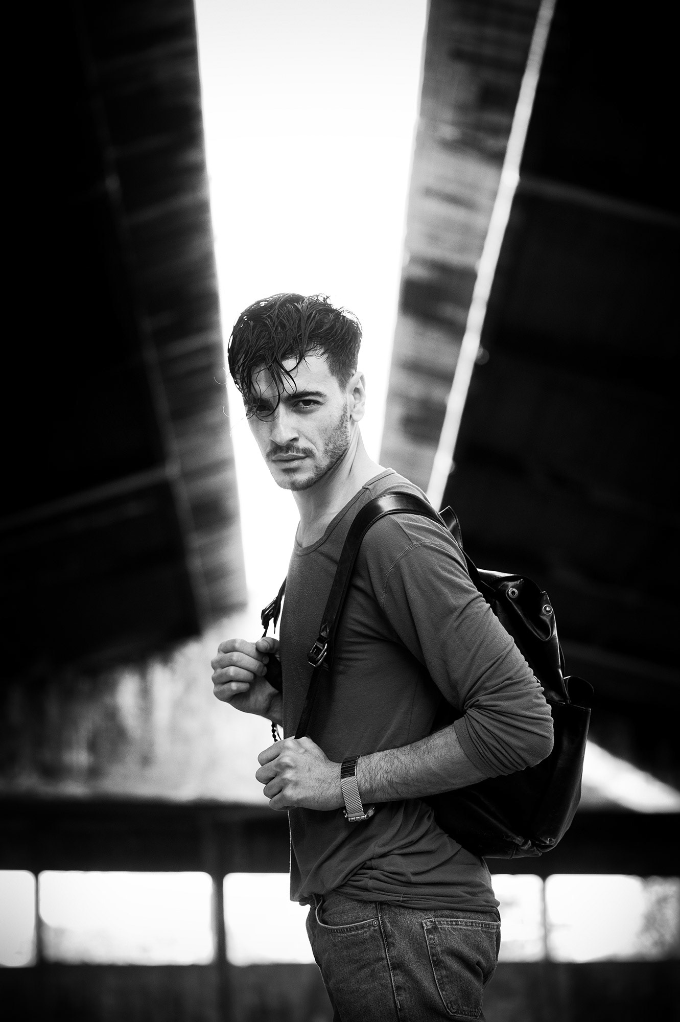 Άνδρας με σακίδιο κοιτάζει τον φακό μέσα σε εγκαταλελειμμένο βιομηχανικό κτίριο, σε ασπρόμαυρη λήψη.     Man with a backpack looks at the camera inside an abandoned industrial building in black and white.