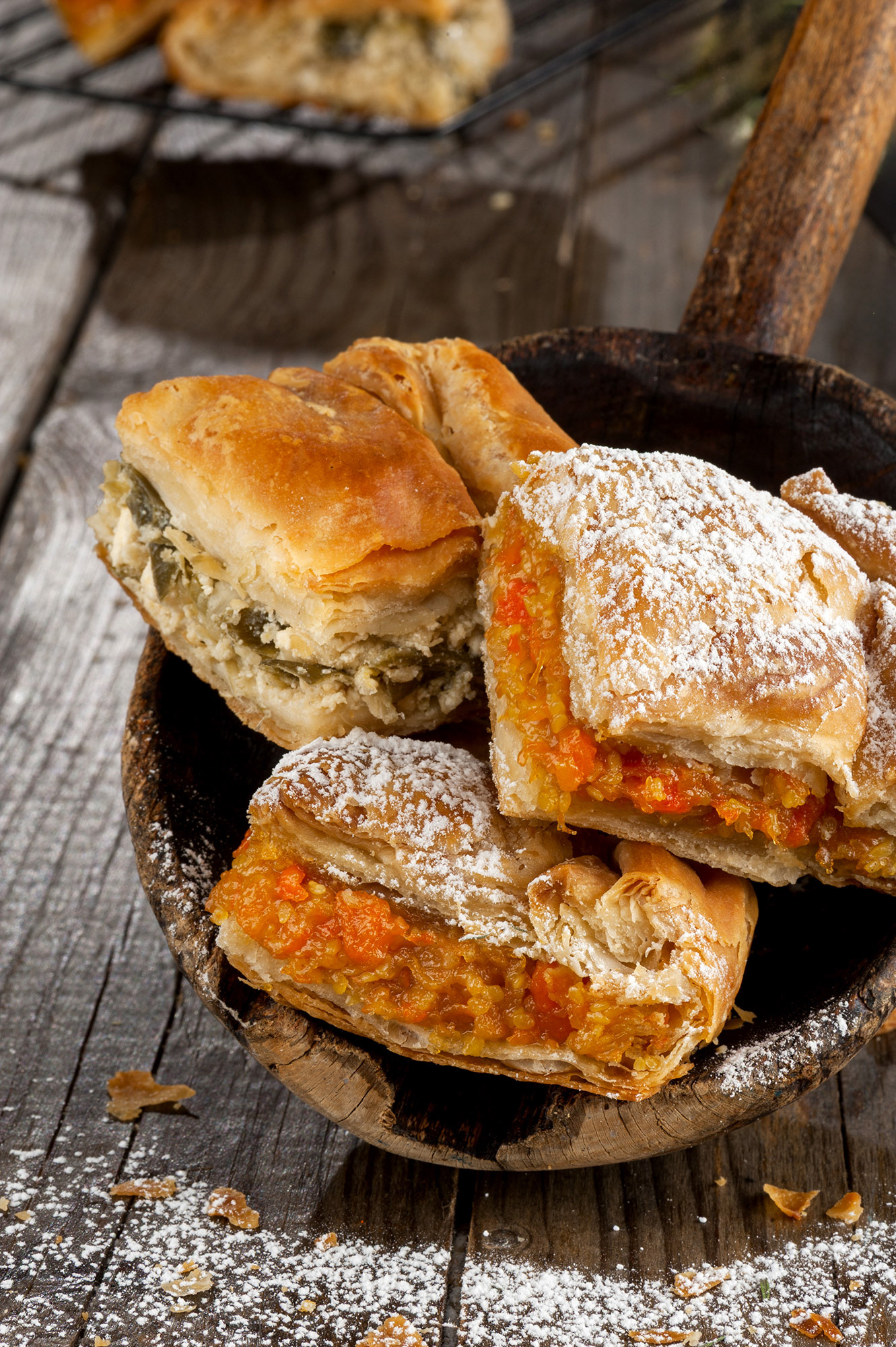 Ρουστίκ food styling με τετράγωνα κομμάτια παραδοσιακής ελληνικής σπιτικής πρασόπιτας, δίπλα σε μια γλυκιά κολοκυθόπιτα πασπαλισμένη με ζάχαρη άχνη επάνω σε ξύλινη σπάτουλα       /  Rustic food styling of square cut pieces of traditional Greek homemade leek pie prasopita, paired with a sweet pumpkin pie sprinkled with powdered sugar on a wooden spatula